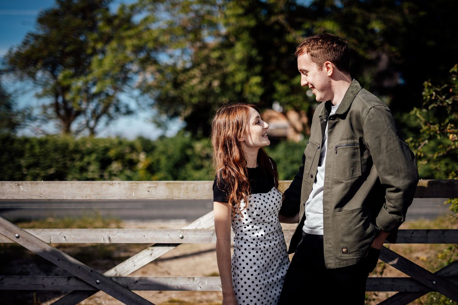 Two people sitting together on a wooden fence in a rural countryside setting.