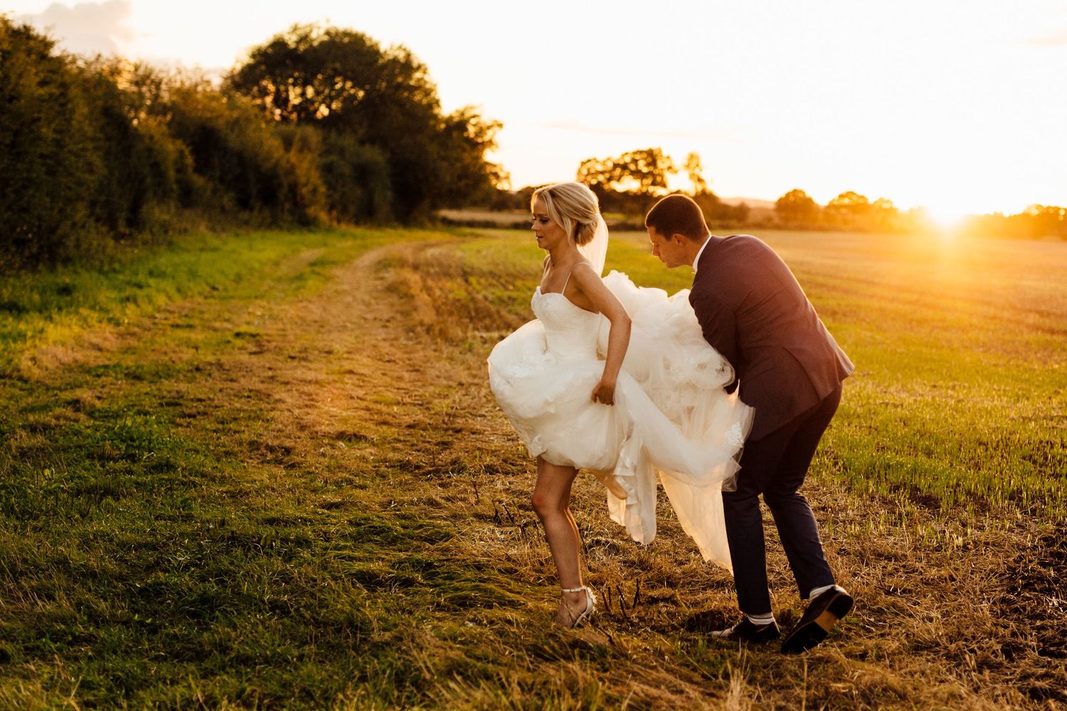 Newlyweds embrace in a golden sunset field during their wedding photoshoot.