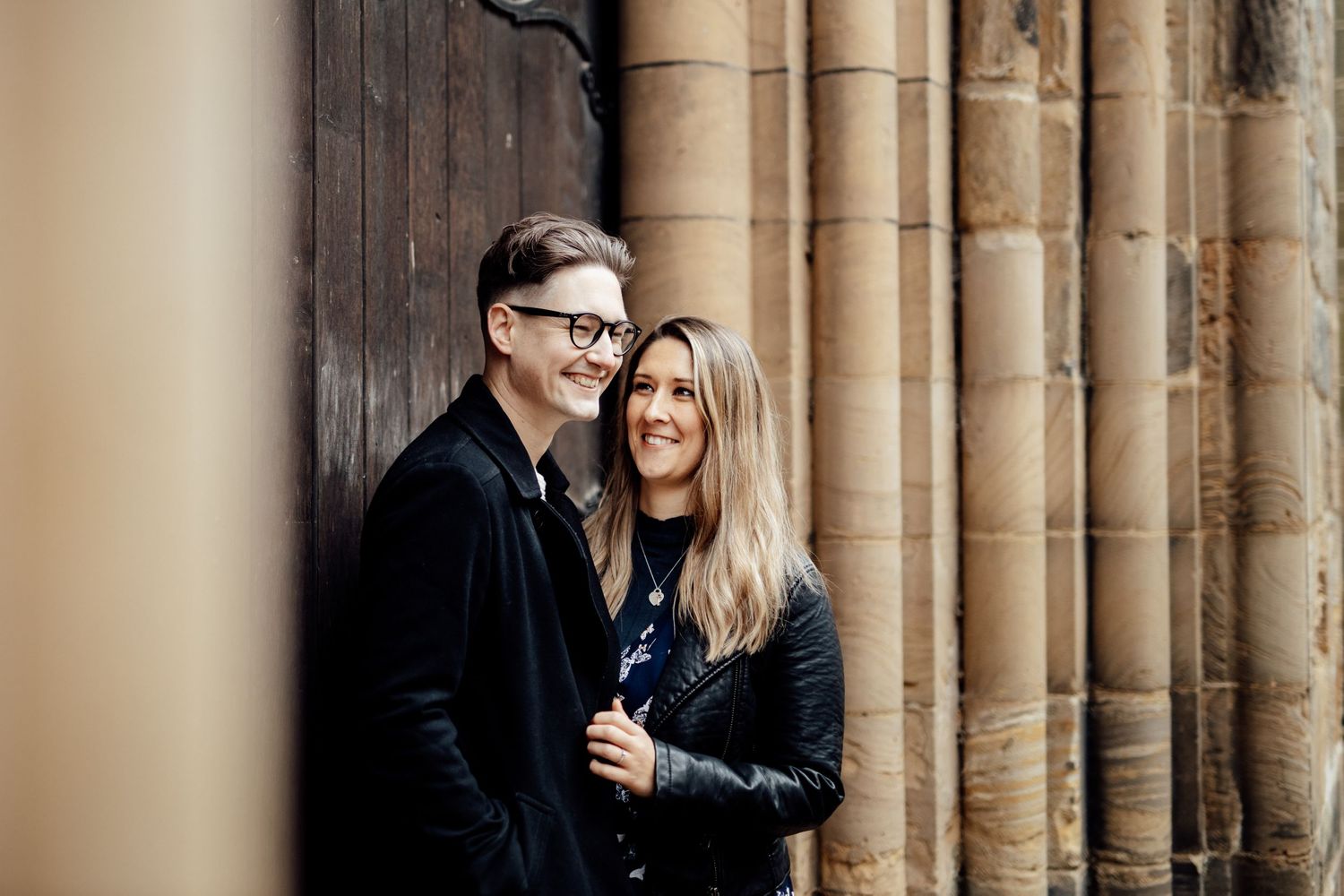 A couple stands close together near classic stone columns in warm lighting.