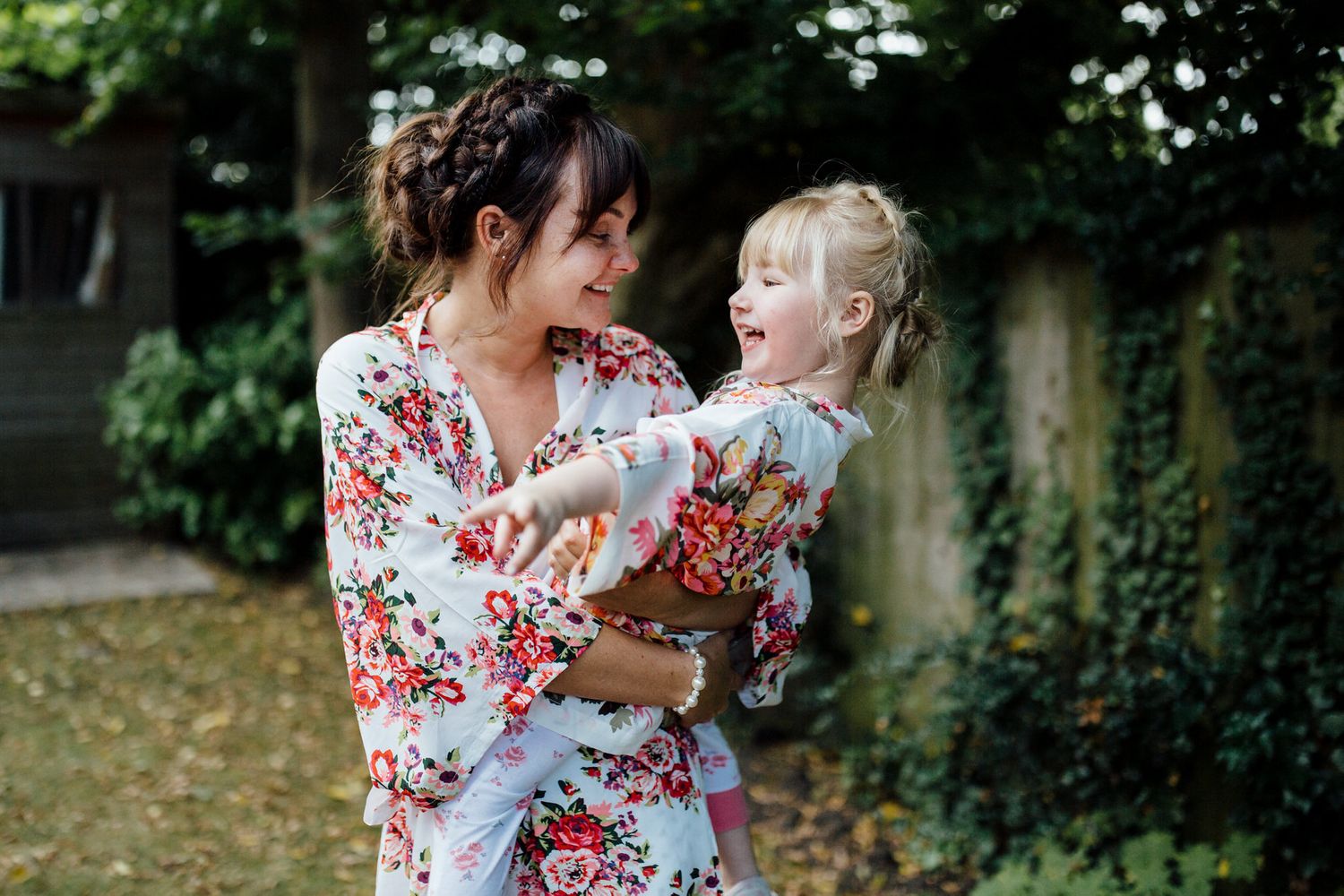 Mother and child share a tender moment in a garden with white flowers.