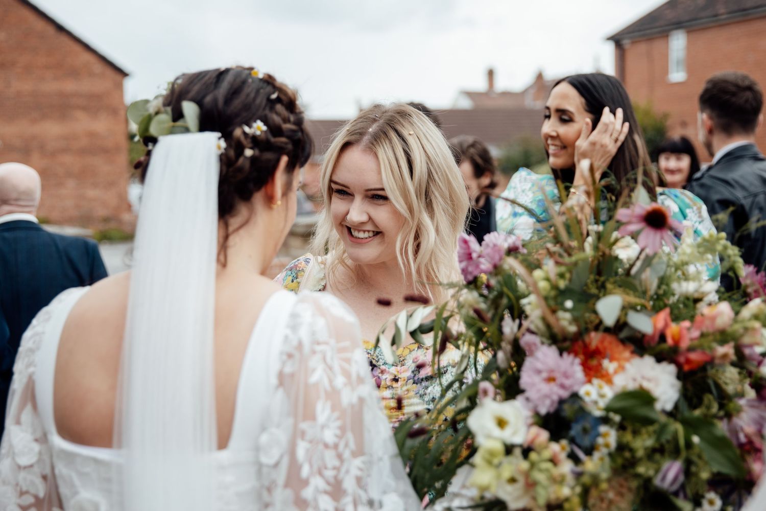 Wedding party members gather outdoors with colorful floral bouquets and arrangements.