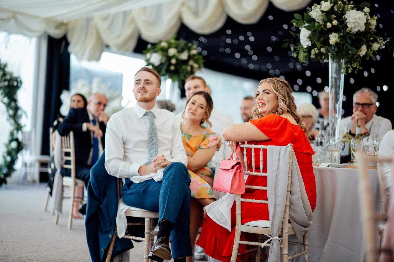 Wedding reception guests enjoying celebrations with decorative white draping and floral arrangements.