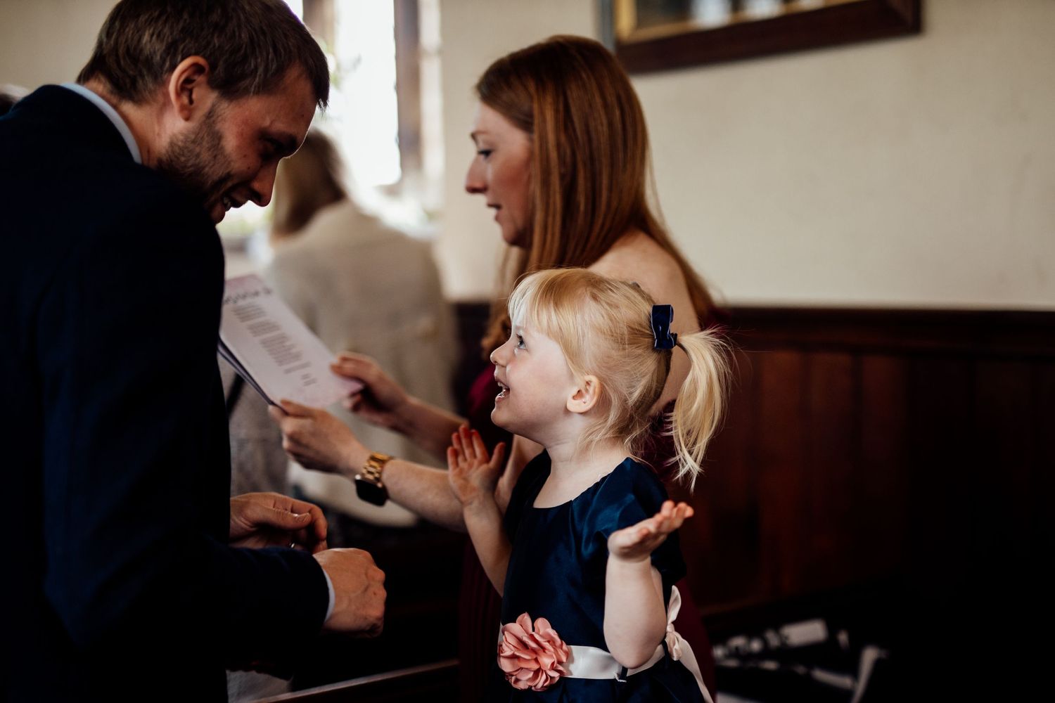 A small child in a navy dress interacts with wedding guests during the celebration.