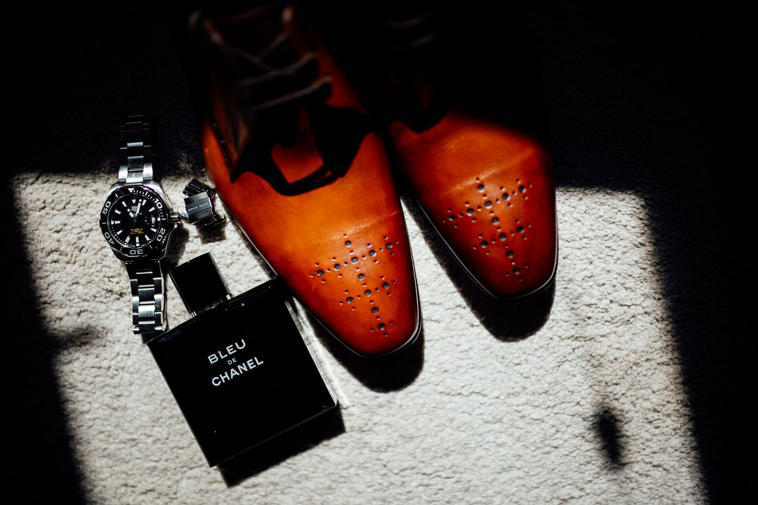 Brown leather dress shoes and watch arranged artistically in dramatic lighting.