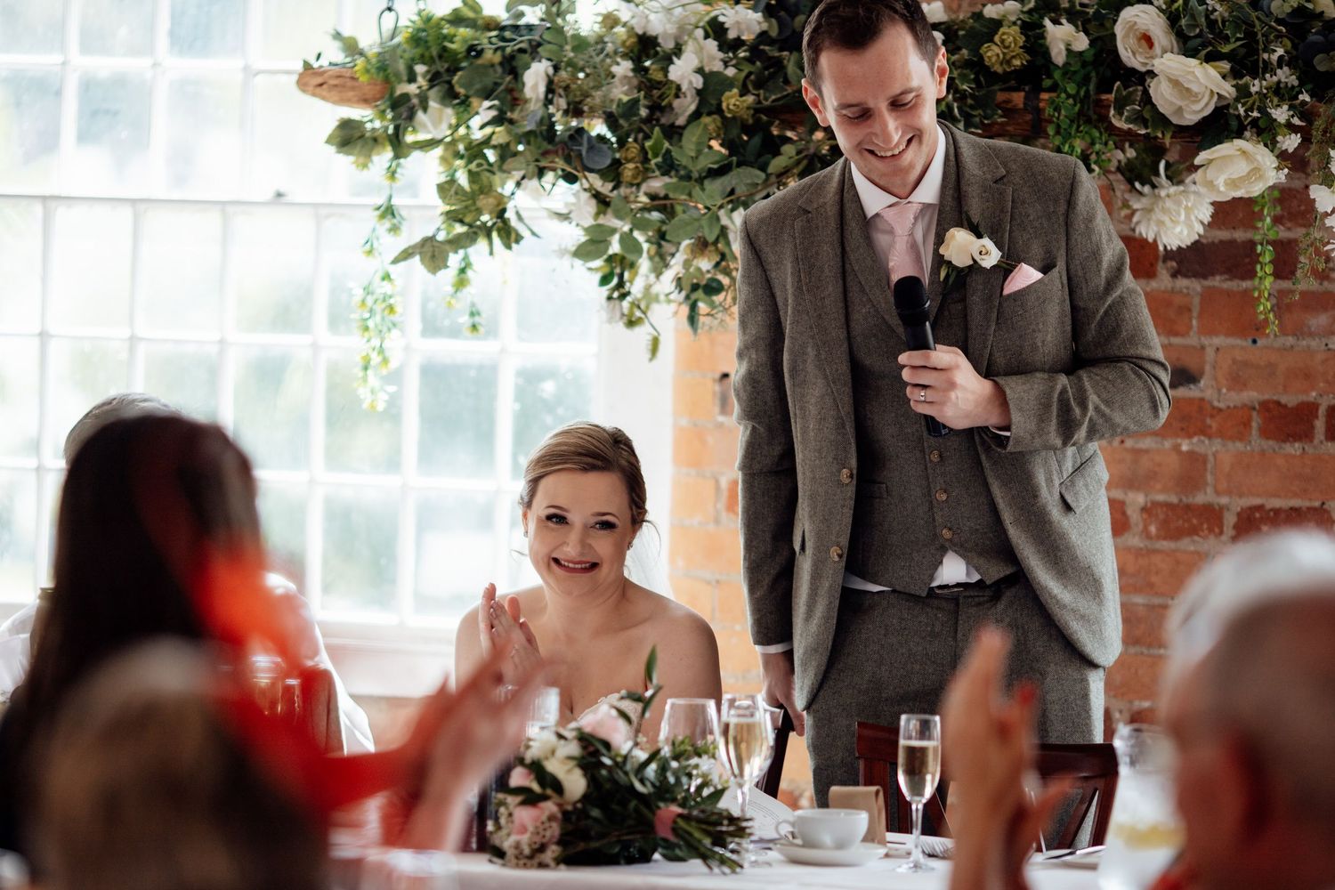 Wedding ceremony space decorated with floral arrangements and greenery in a bright sunlit room.