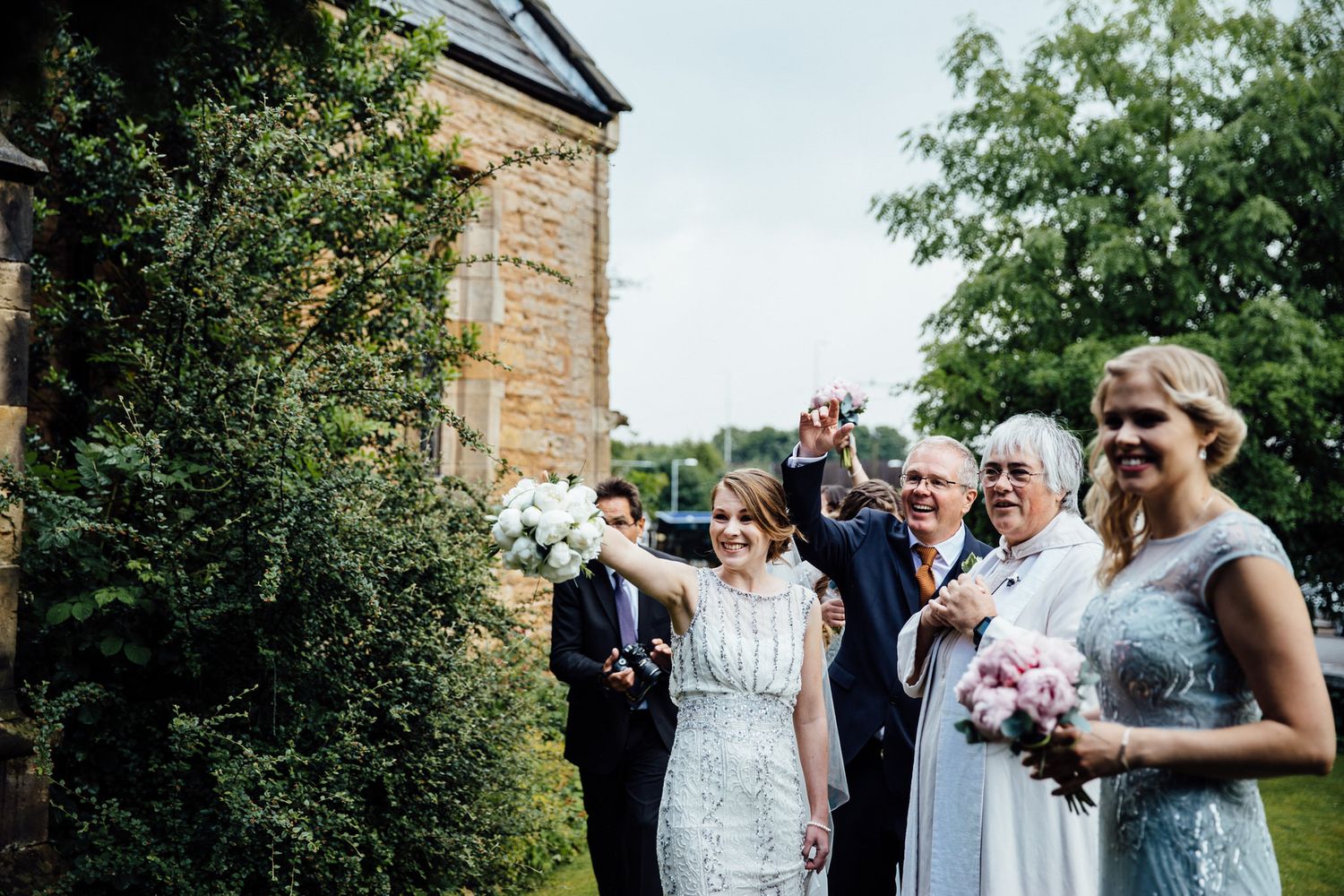 Wedding party celebrates with confetti and joyful expressions outside a stone church building.