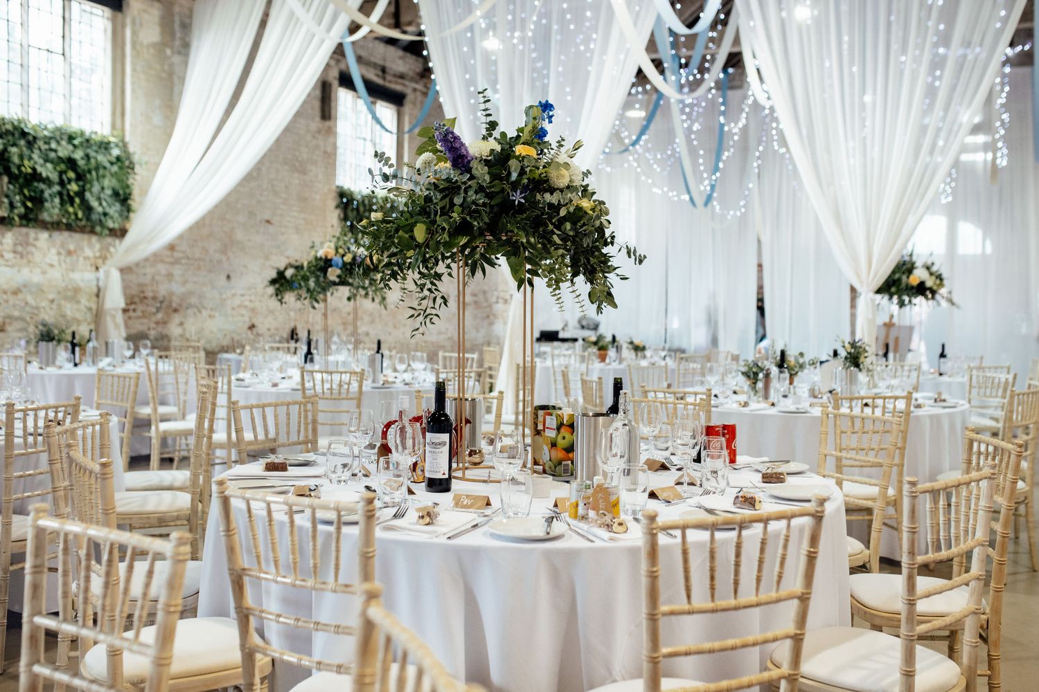 Elegant wedding reception venue with white draping, fairy lights and chiavari chairs.