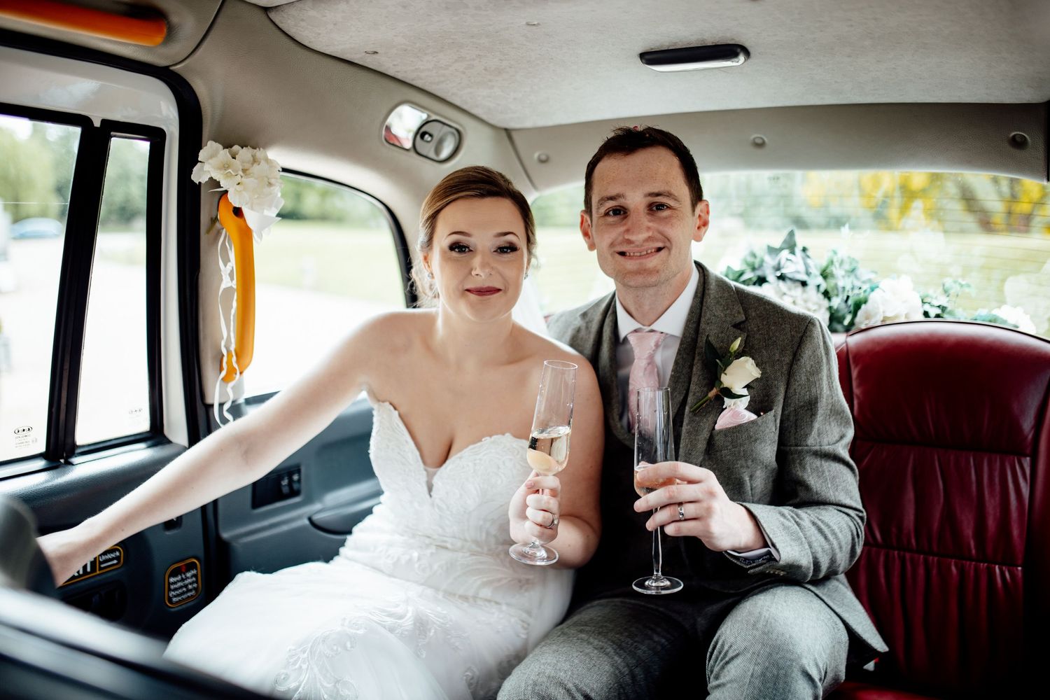 Wedding couple shares champagne toast in classic car backseat.