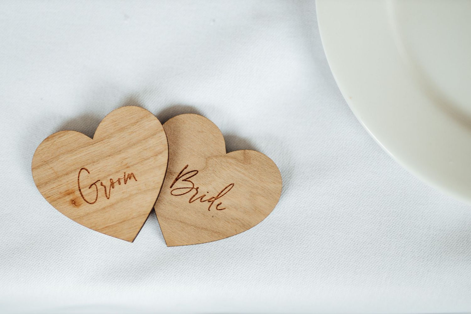 Wooden heart-shaped wedding decorations displayed on white table settings.