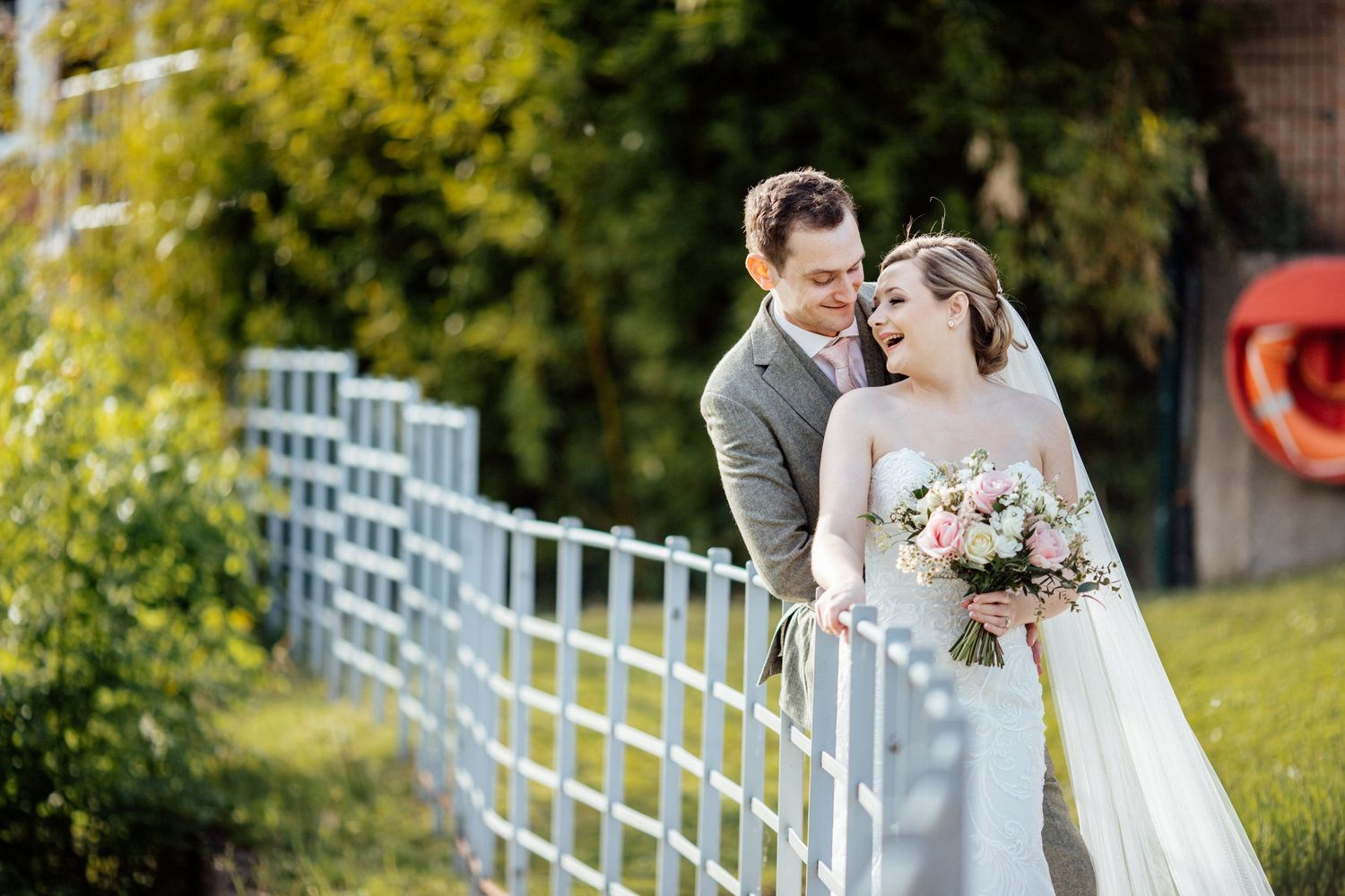 Couple sharing romantic moments along a white railing with lush greenery in background.