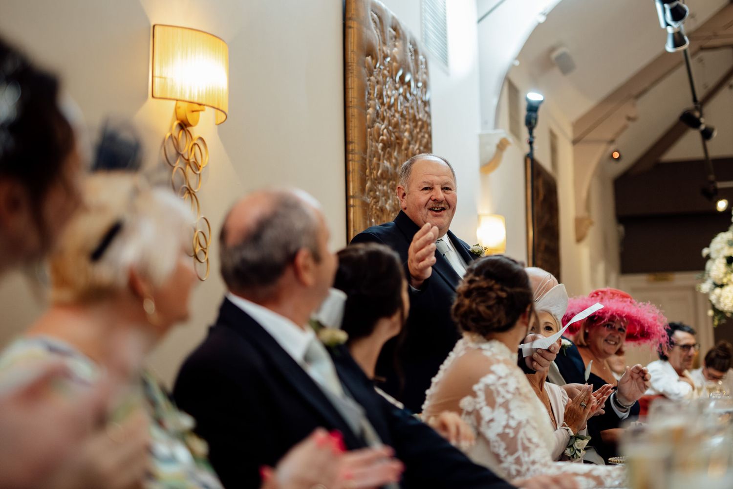 Wedding reception guests seated at elegant tables with warm lighting and decorative centerpieces.