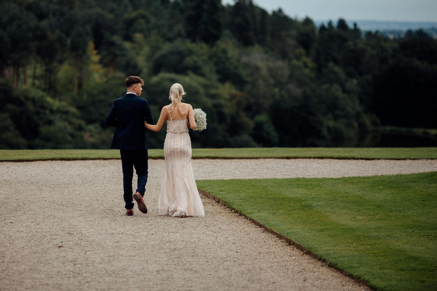 Wedding couple walking through a scenic garden path with rolling hills in background.