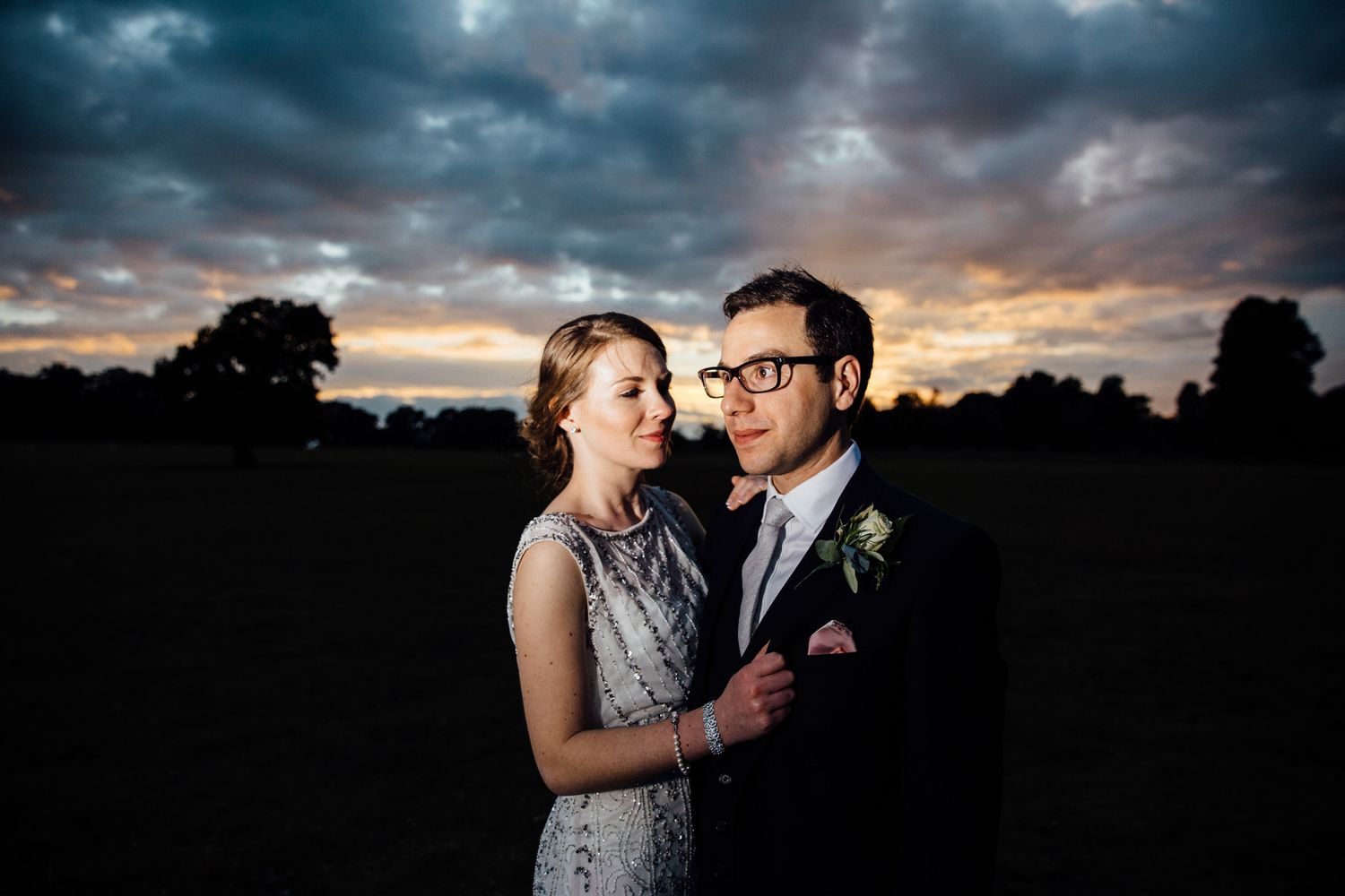 Intimate portrait of newlyweds embracing at dusk with stormy clouds in background.