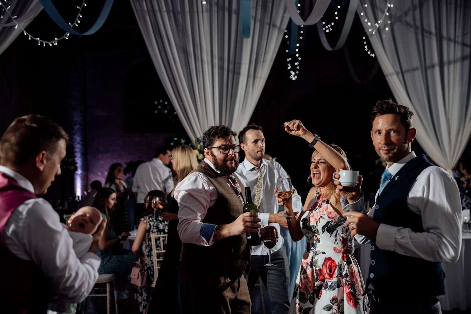 Celebration in a dimly lit venue with white drapes and dancing guests.