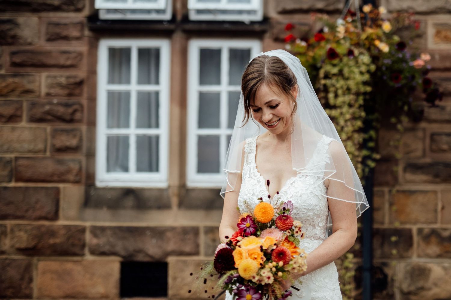 Bride holds colorful autumn bouquet against rustic stone building backdrop.