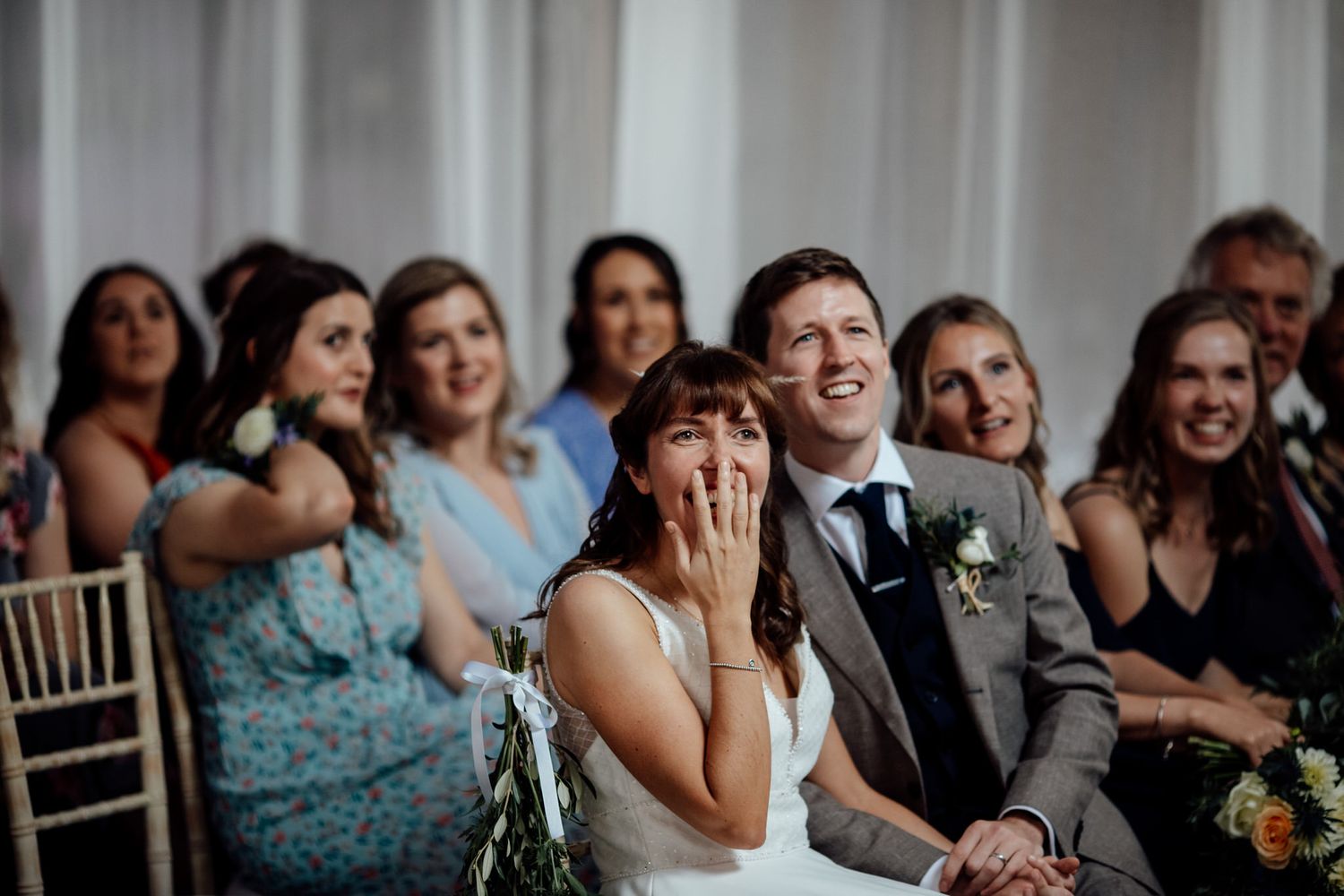 Wedding ceremony guests watching with emotional expressions from white chairs.