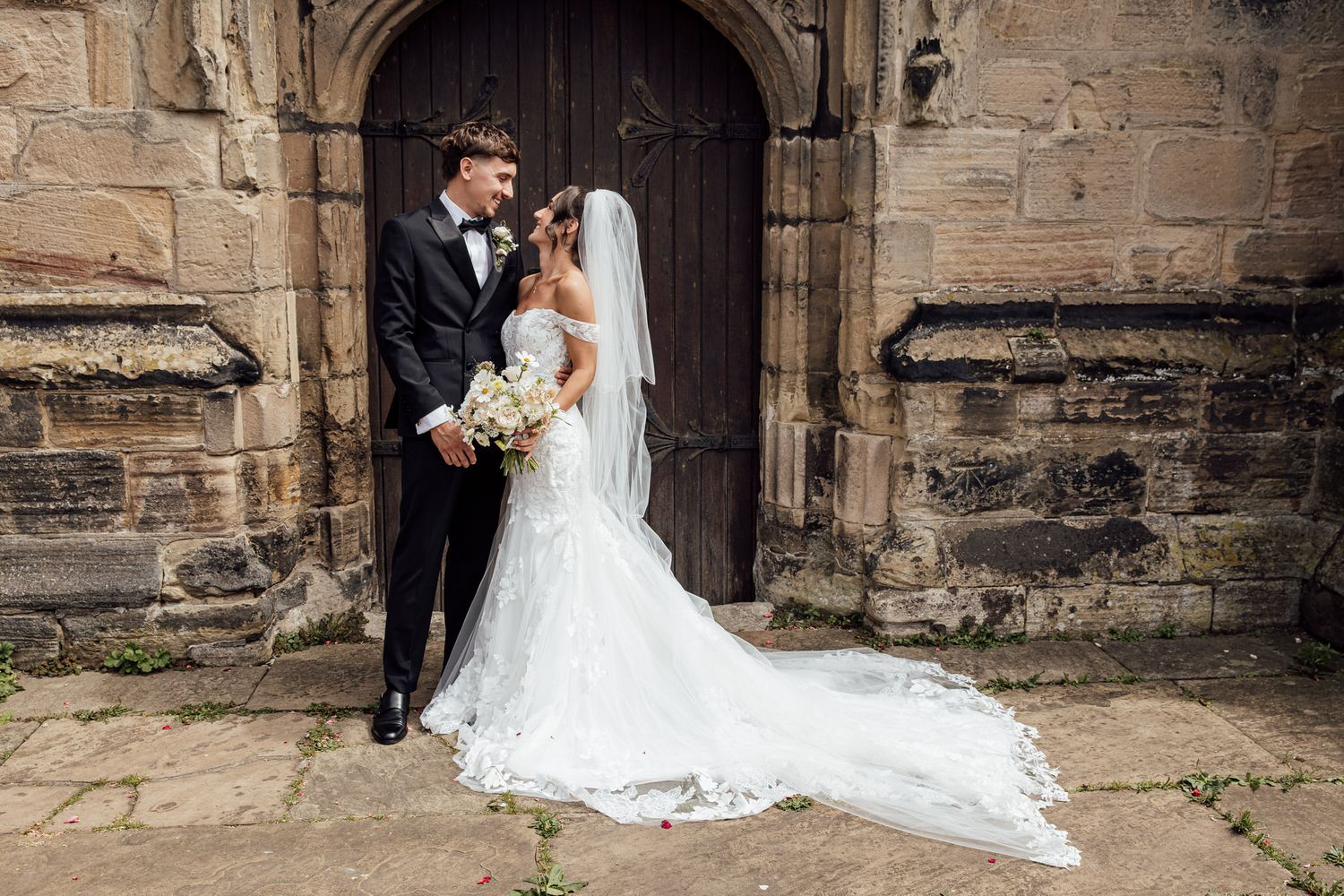 Wedding portrait in front of historic stone church with ornate wooden door.