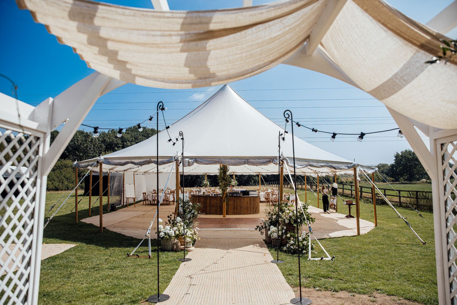 White tent canopies set up outdoors for wedding reception with string lights and lattice details.