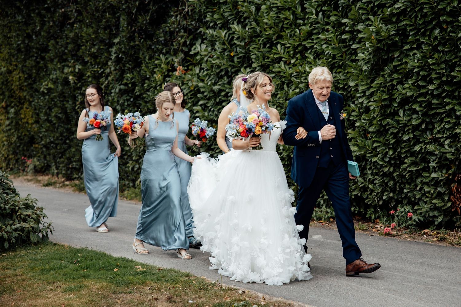 Wedding party walking along garden pathway during outdoor celebration.