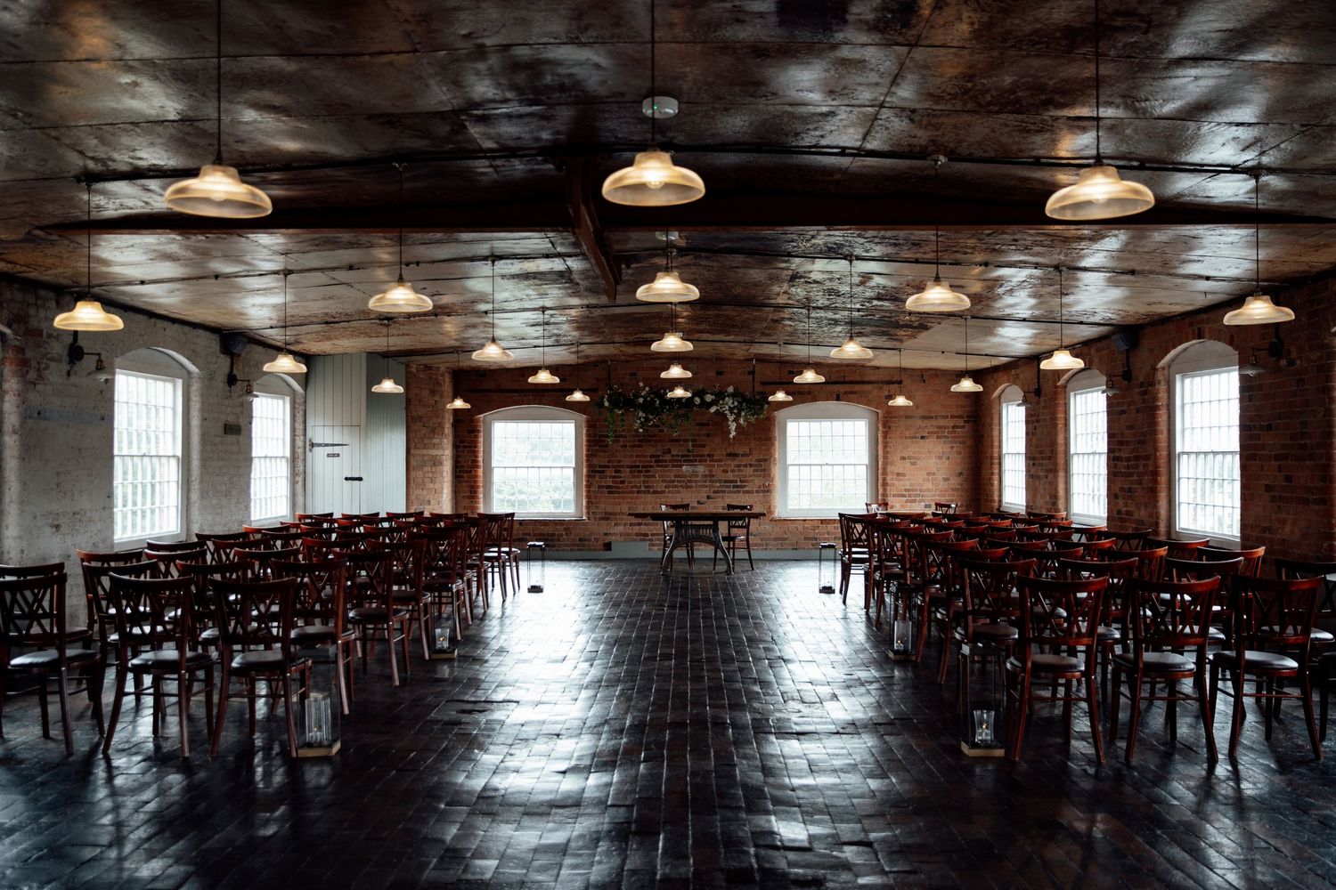 Empty wedding ceremony venue with dark wood floors and pendant lighting.