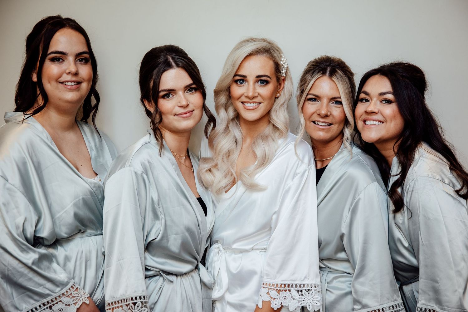 Bridal party wearing matching silver robes pose together indoors.