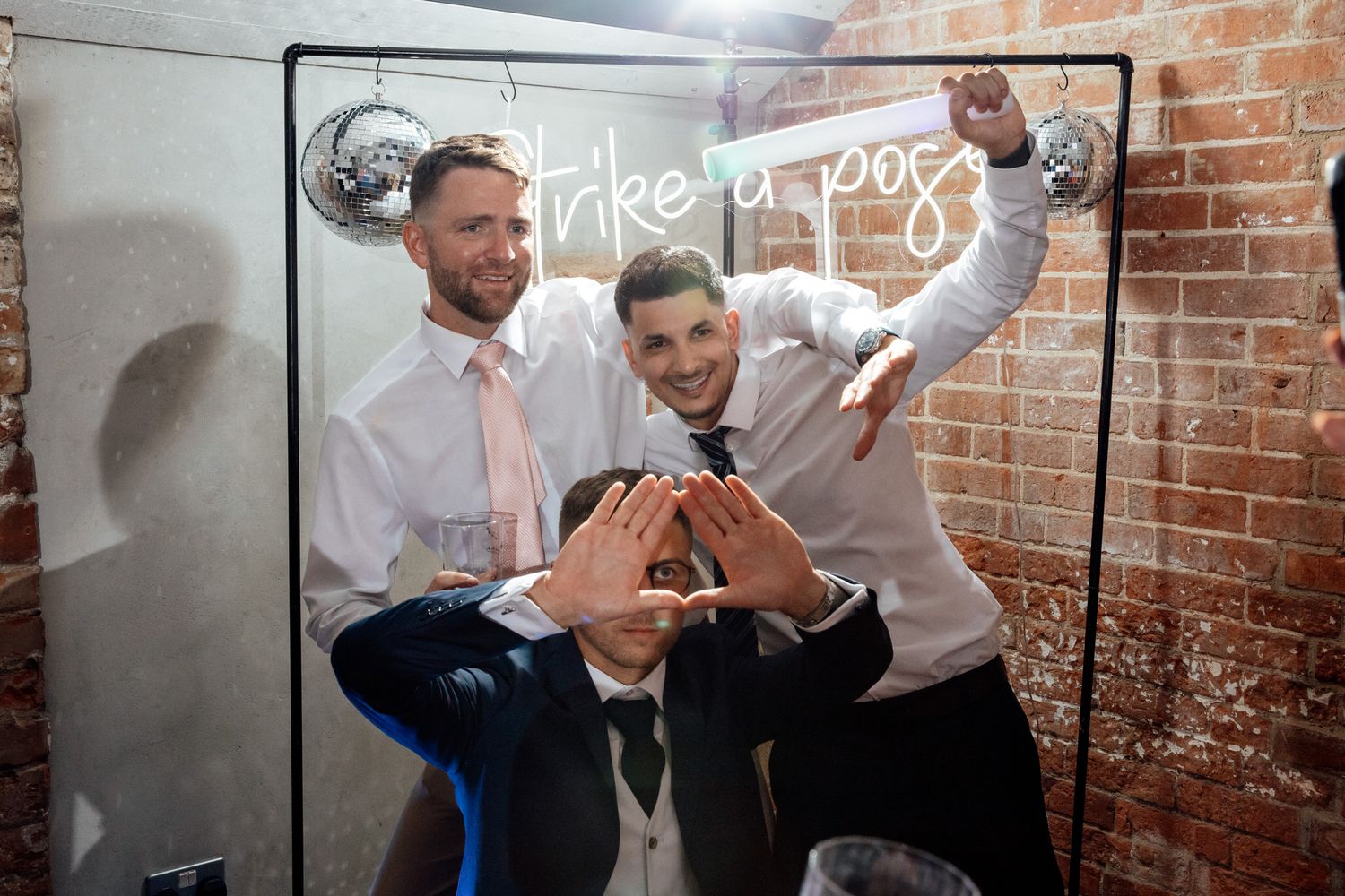 Wedding guests celebrate with drinks and dancing in an industrial-style brick venue.