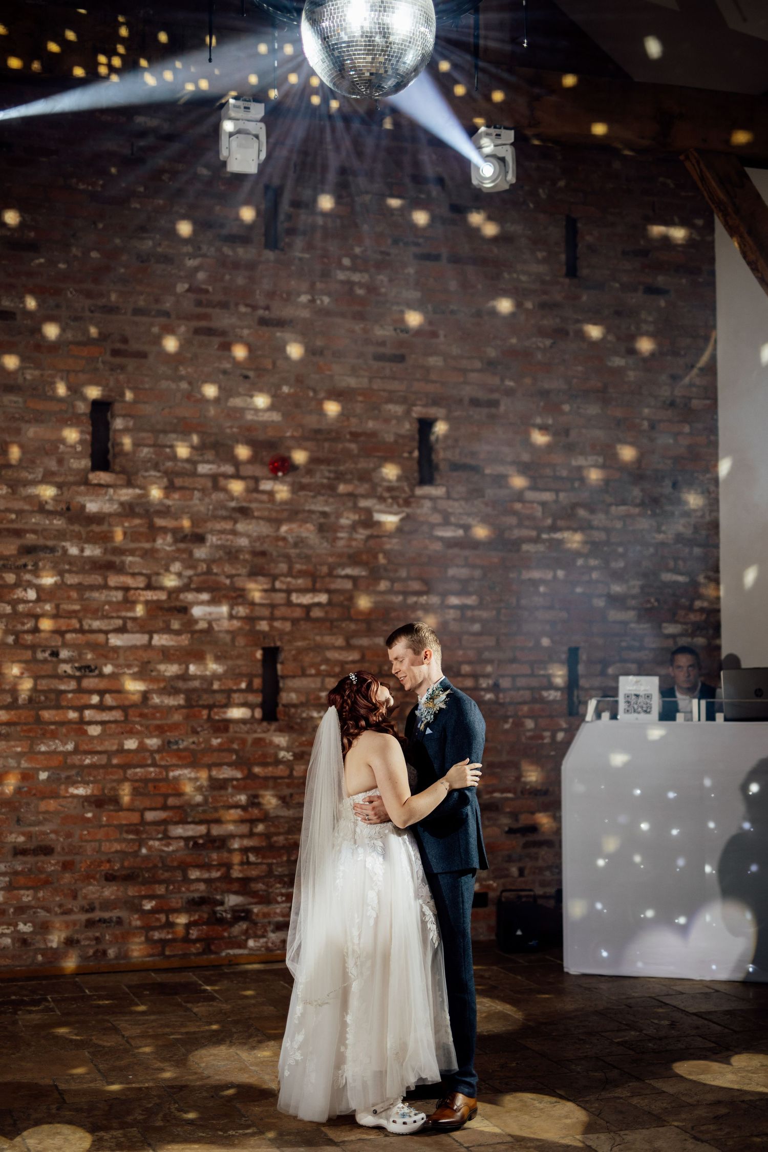 Couple dancing under disco ball and string lights in rustic brick venue.