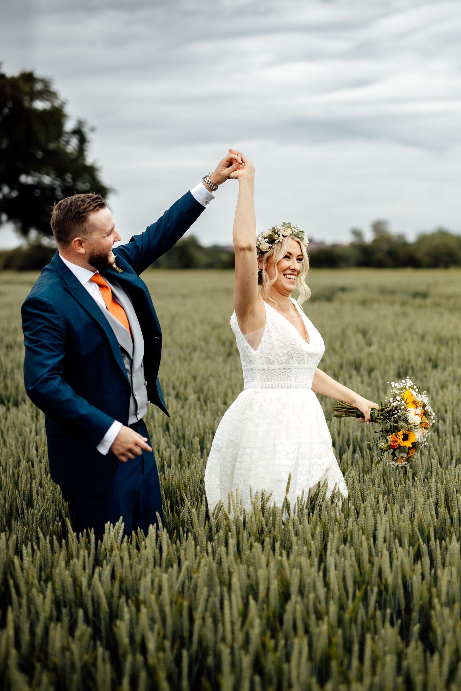 A celebratory couple pose joyfully in a wheat field during their wedding photoshoot.