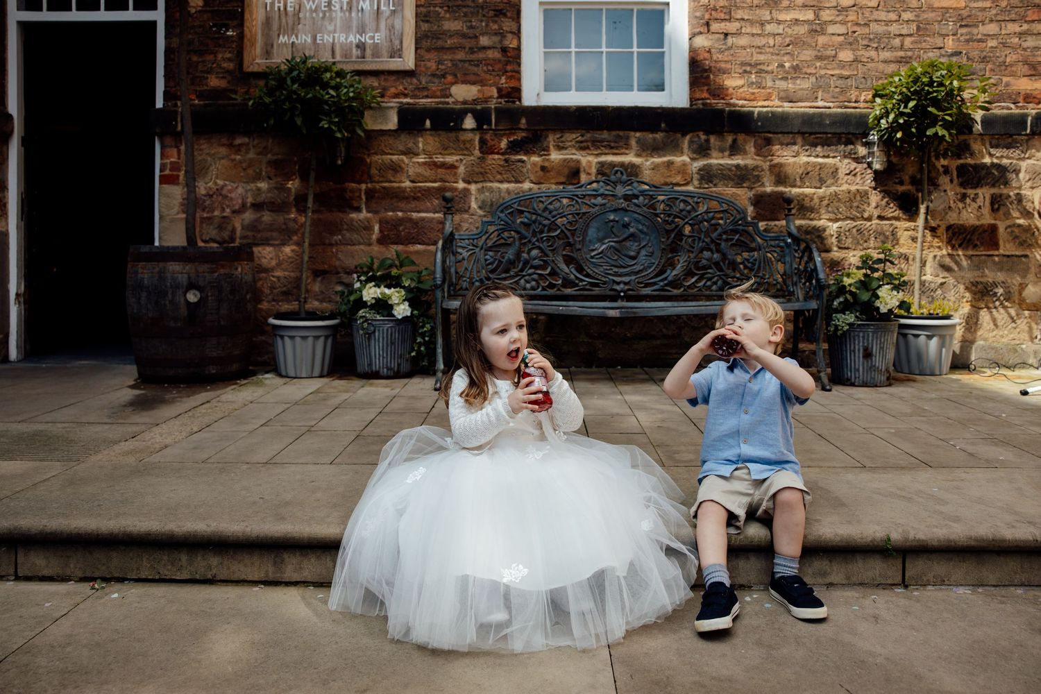 Wedding party relaxing on stone steps outside historic brick building.