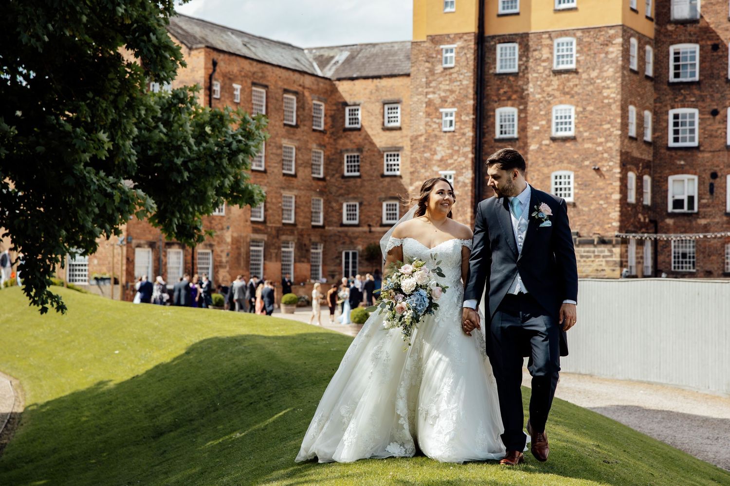 Wedding party walking along brick building path on sunny afternoon.