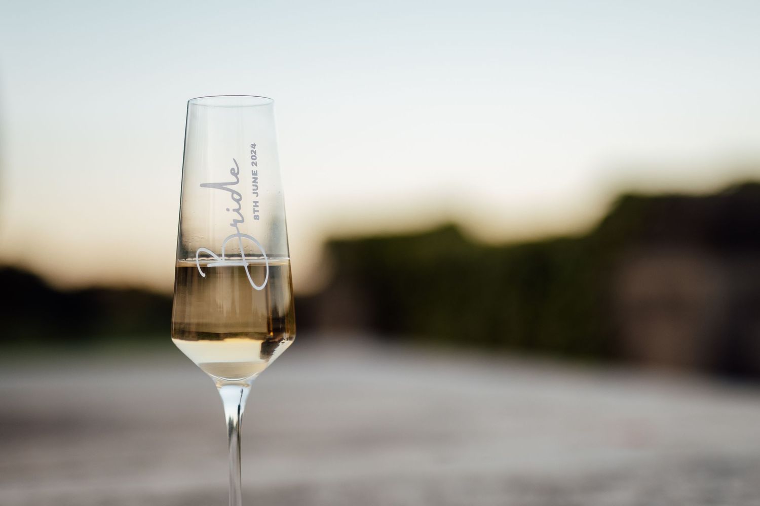 Champagne flute with blurred sunset background at outdoor wedding reception.