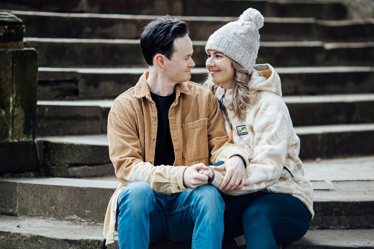 Couple sitting on stone steps wearing matching tan and white winter outfits.