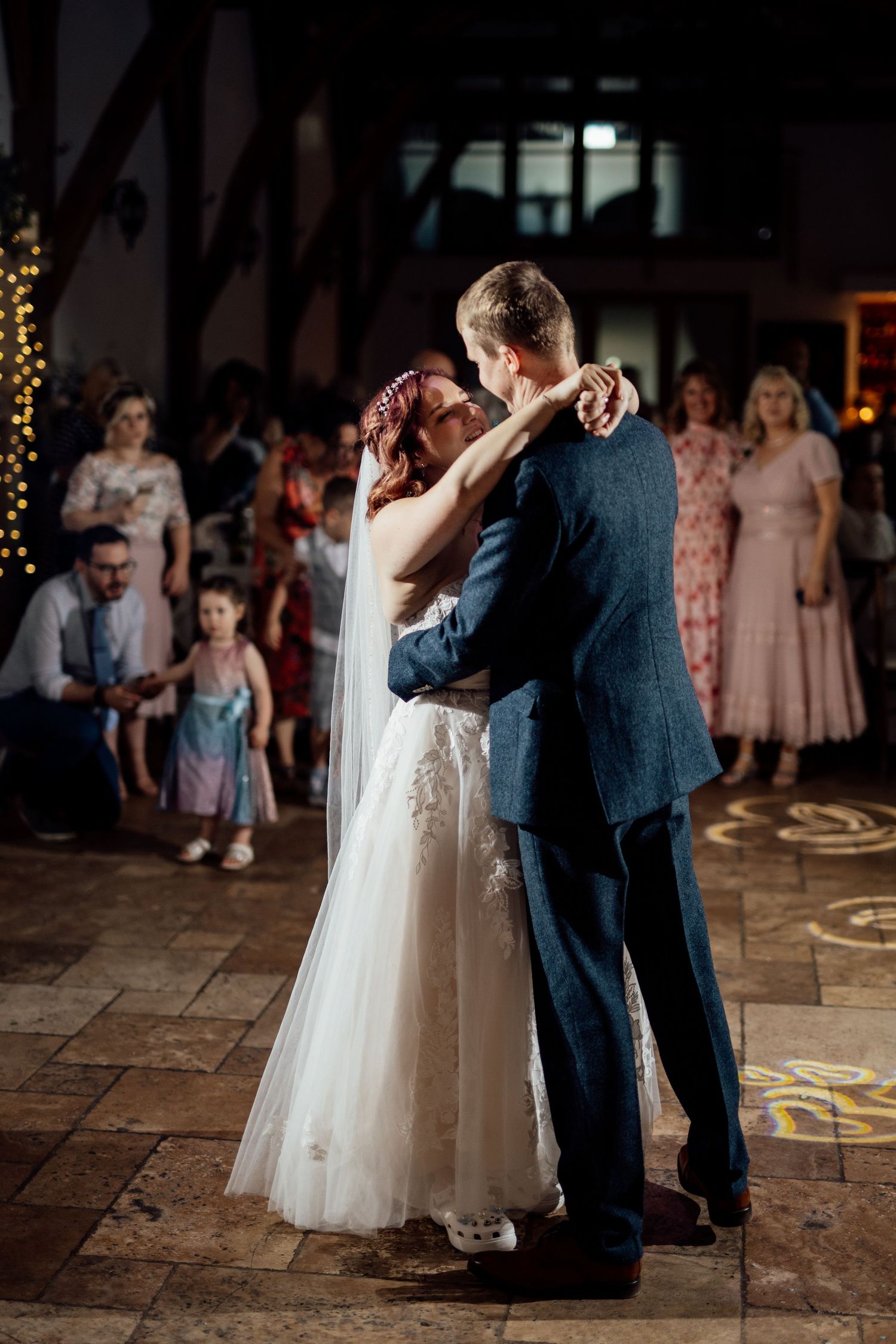 Couple shares their first dance at wedding reception on stone floor with romantic lighting.