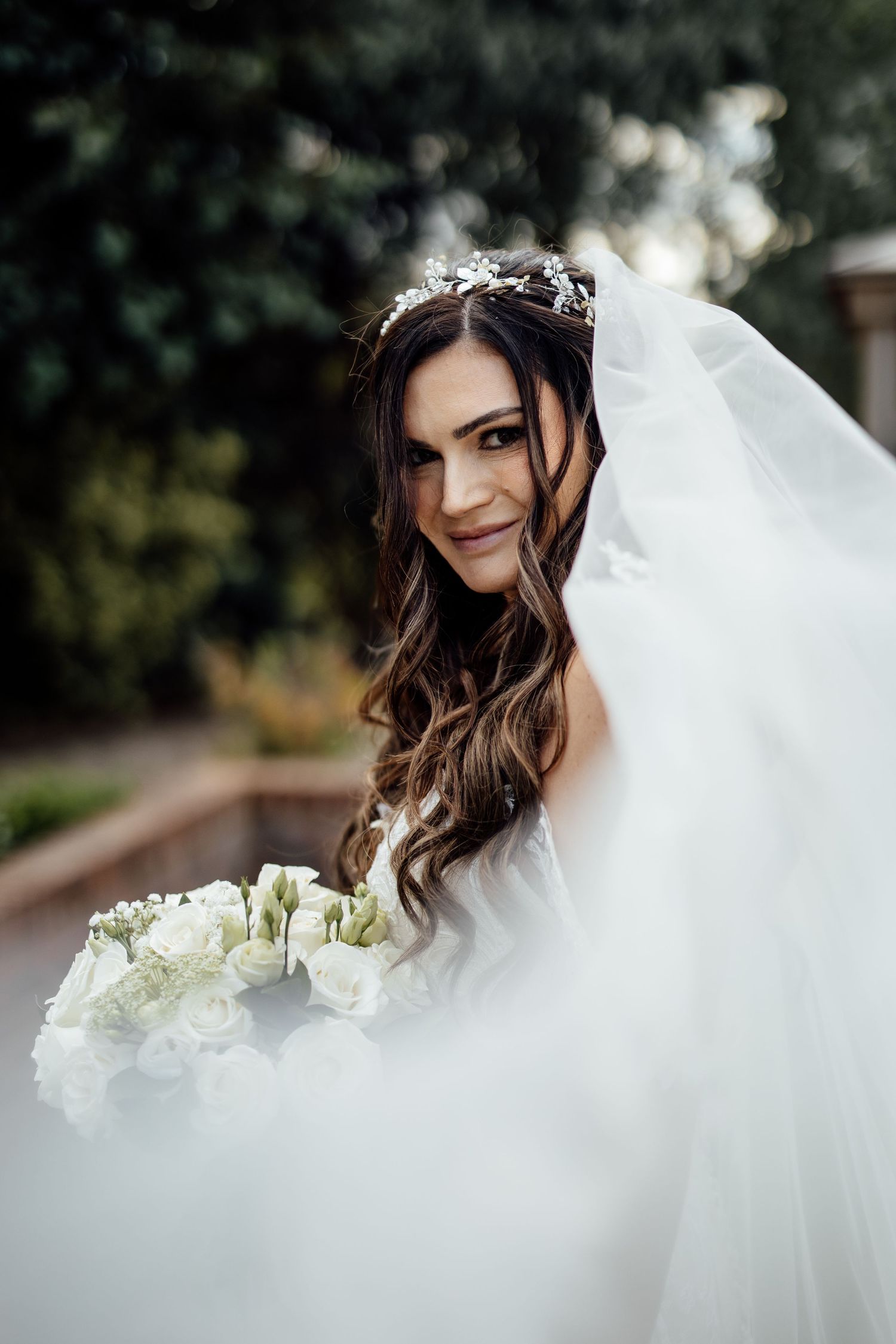 Ethereal bridal portrait with flowing white veil and bouquet.