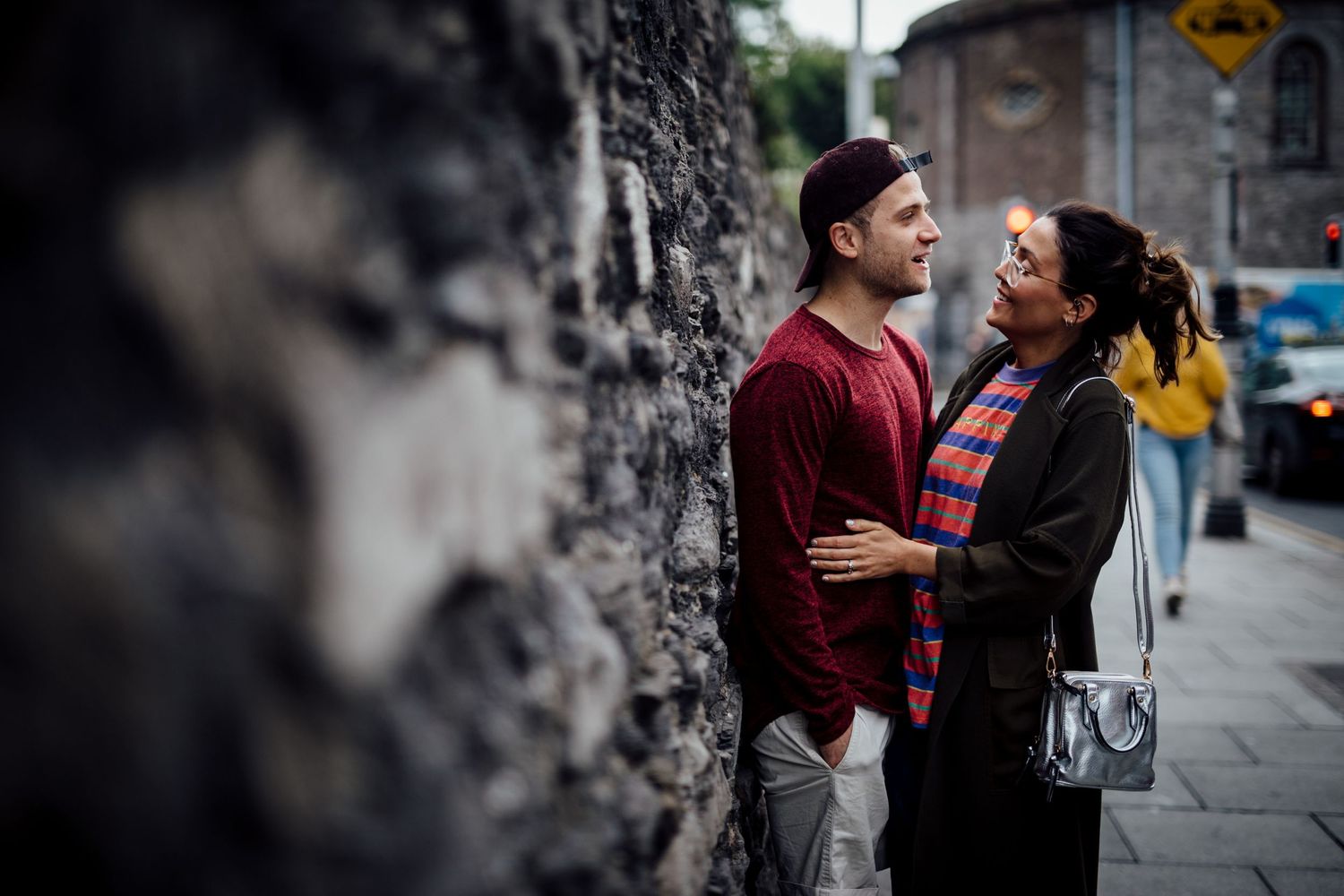 Urban engagement photos with textured stone wall and street signs in background.