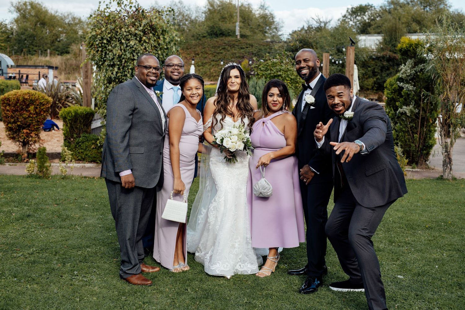 Wedding party posing together on a sunny lawn with formal attire.