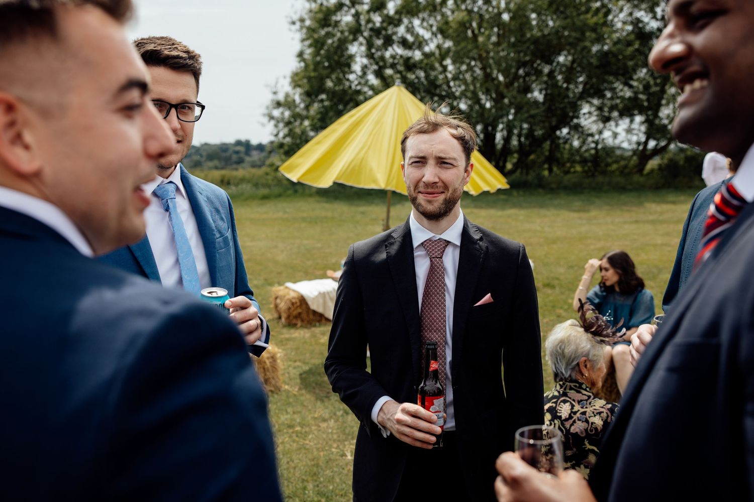 Guests mingle outdoors at a wedding reception with yellow umbrellas visible in the background.