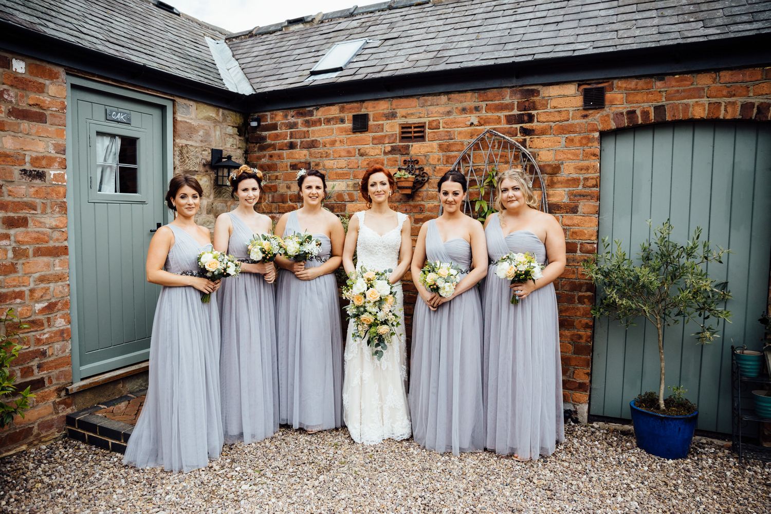 Wedding party in lavender dresses pose together against rustic brick wall.