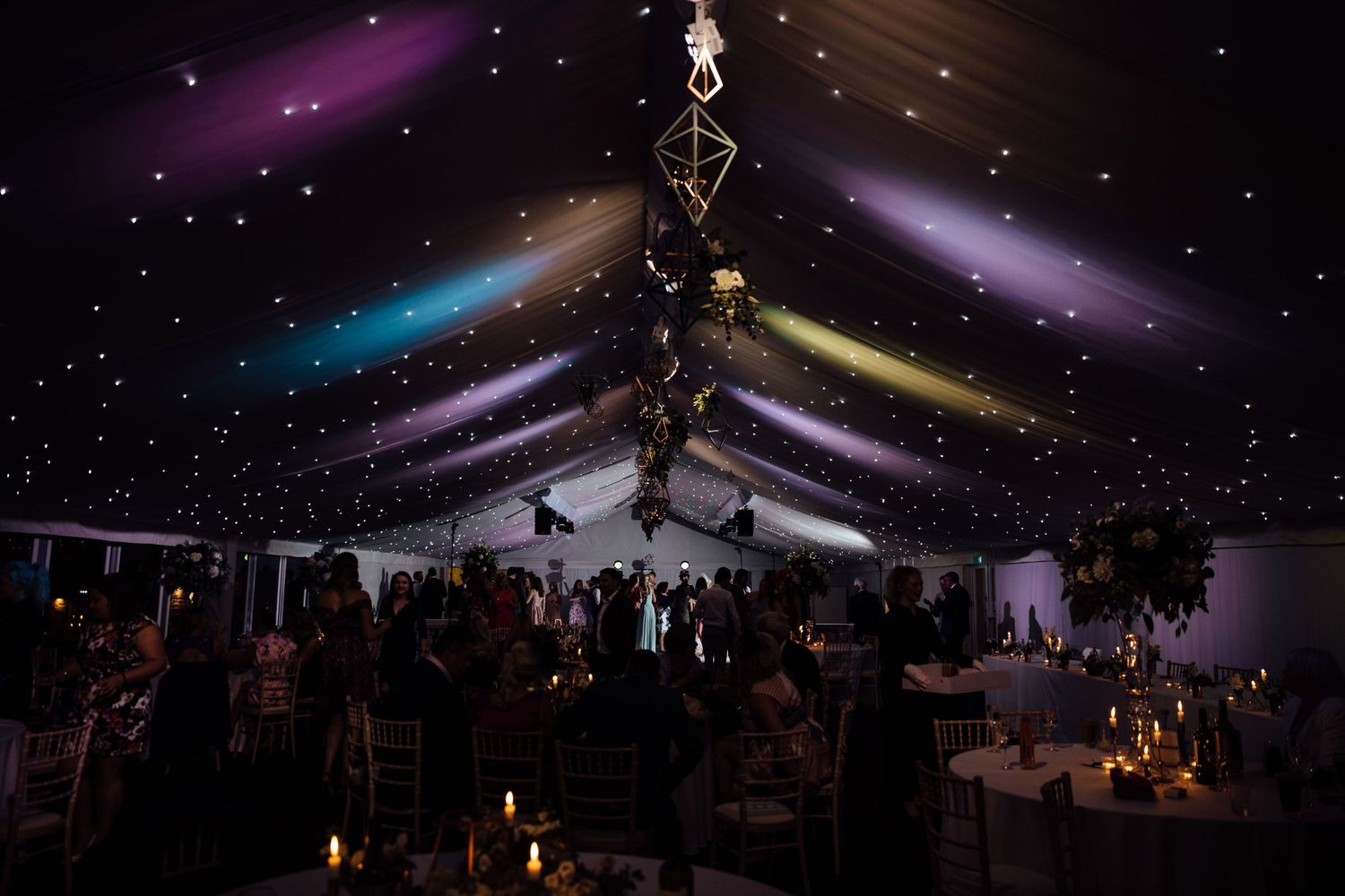 Elegant wedding reception venue with dramatic purple and blue lighting effects on the ceiling.
