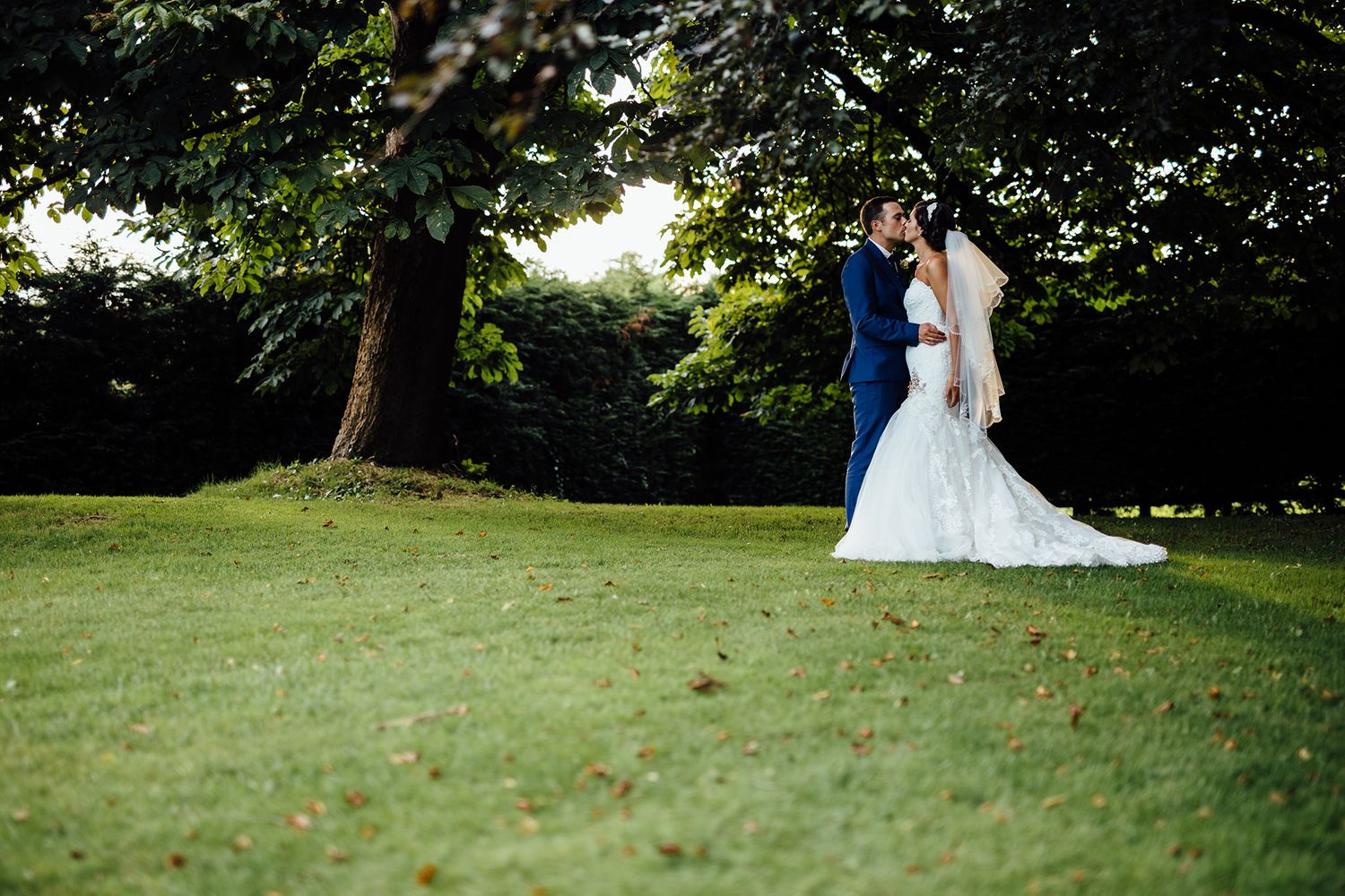 Wedding couple portraits taken on a lush green lawn with trees in the background.