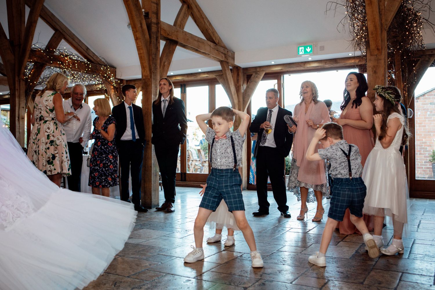Young boy dances energetically at wedding reception in rustic barn venue with exposed beams.