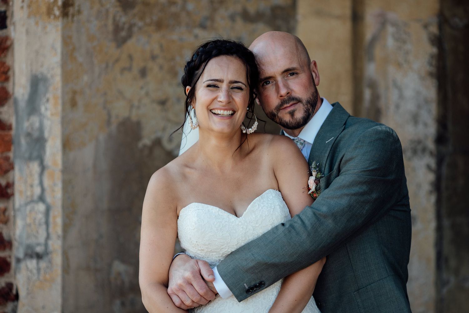Wedding couple embracing against rustic stone wall background.