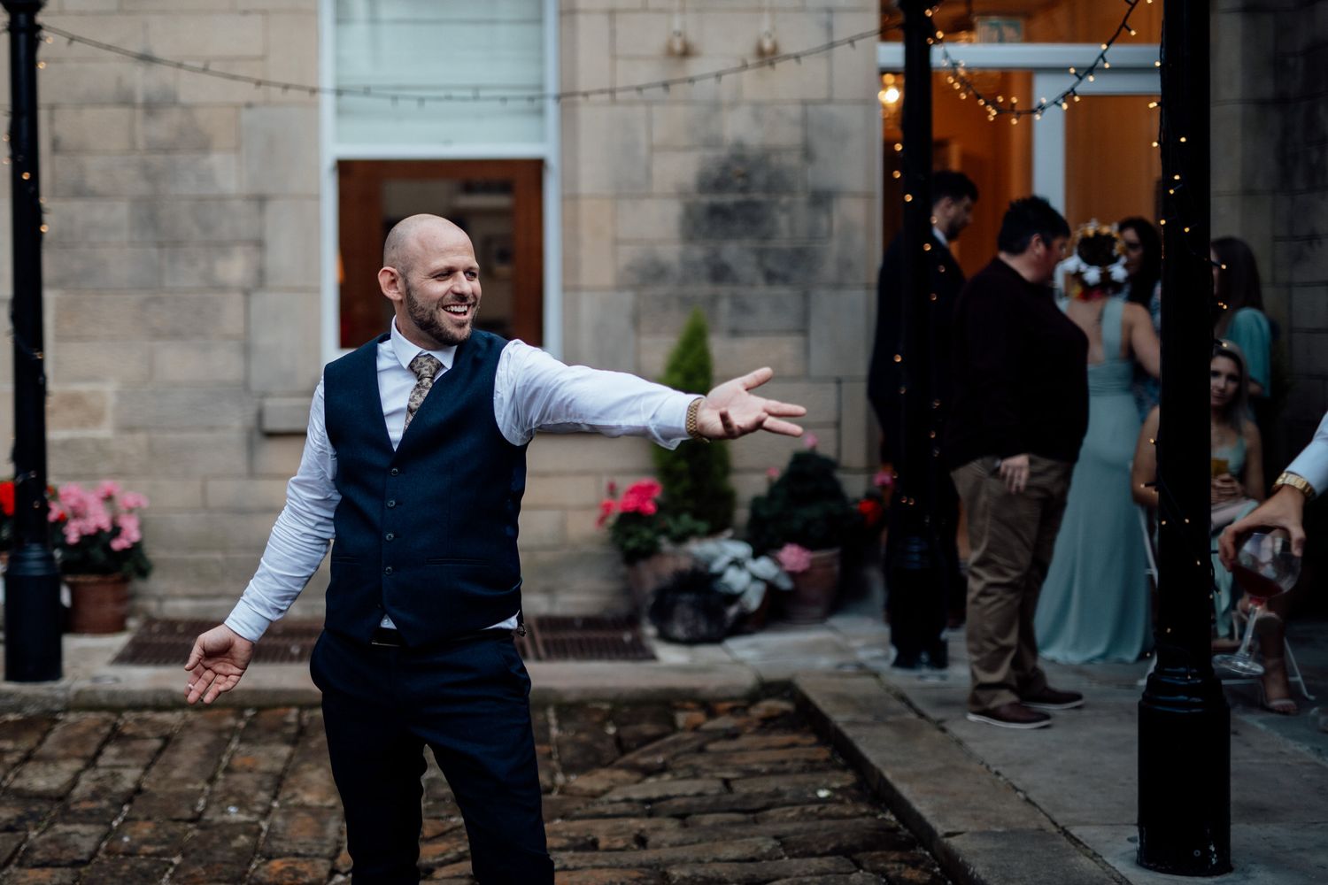 Wedding party members celebrate joyfully outside a stone building entrance.