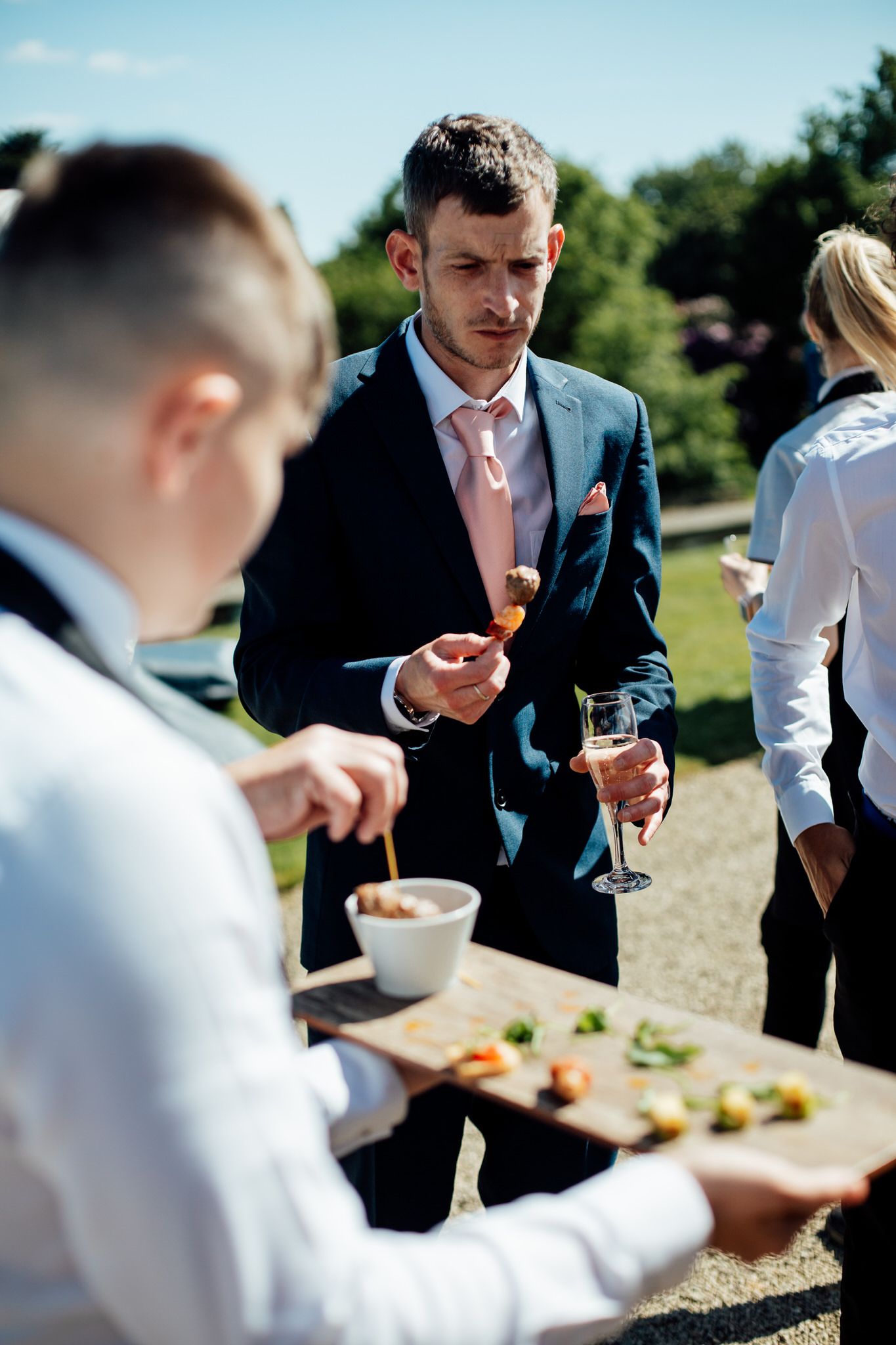 Wedding guests being served canapés and drinks during outdoor reception.