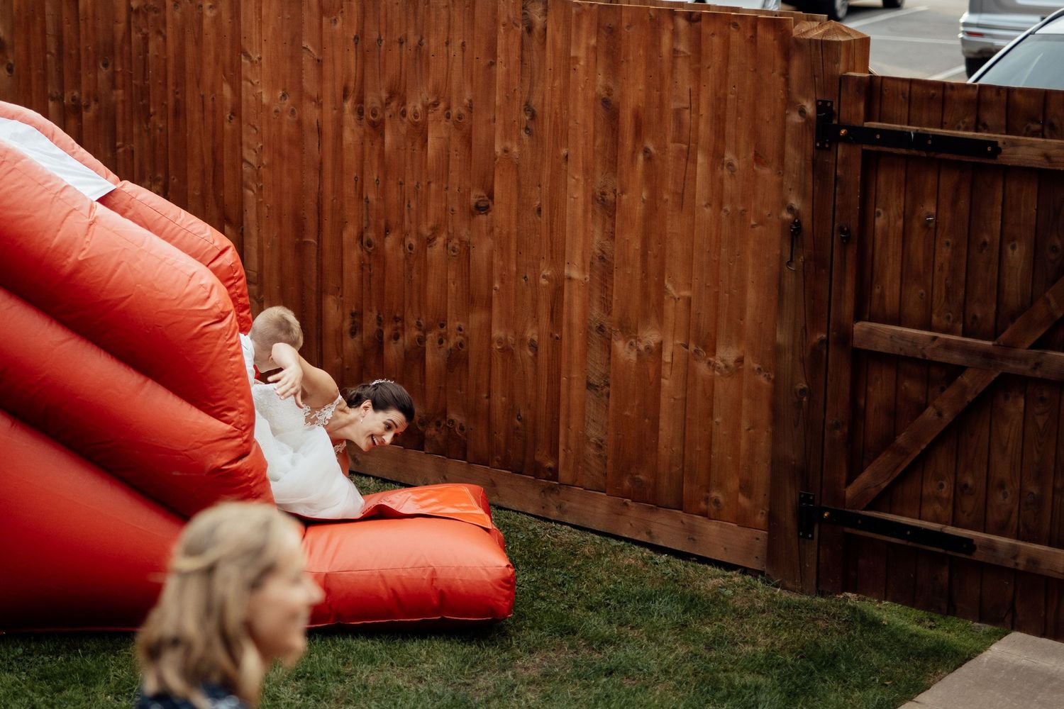 Wedding couple poses playfully near a red bounce house in a backyard setting.