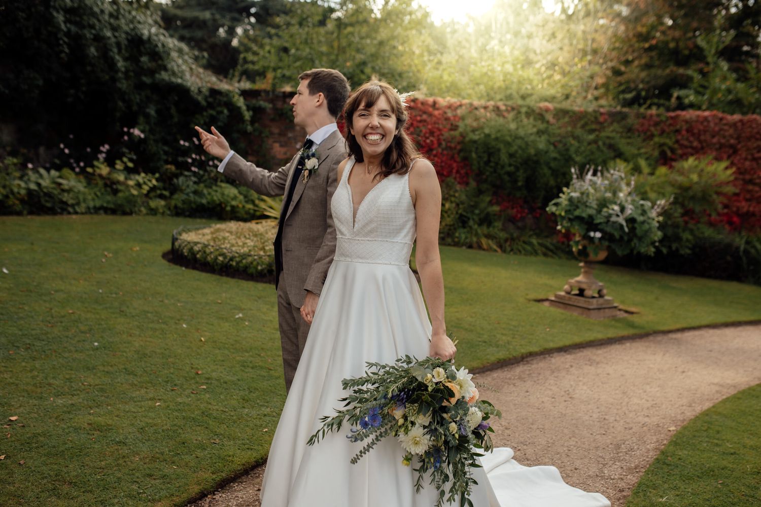 Wedding couple walking along garden path surrounded by lush greenery and flowers.