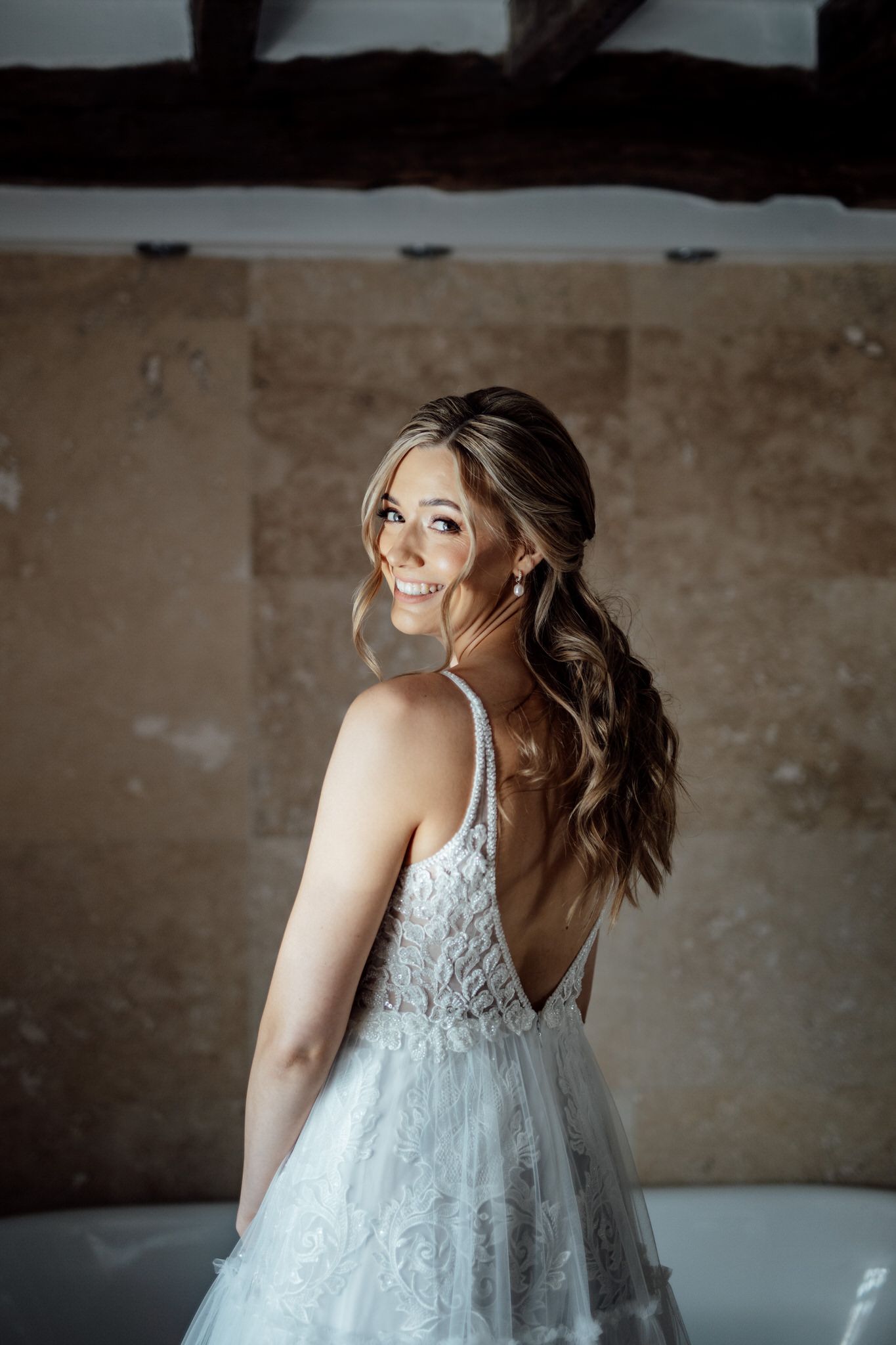 A bride in a lace wedding gown poses against a textured stone wall background.