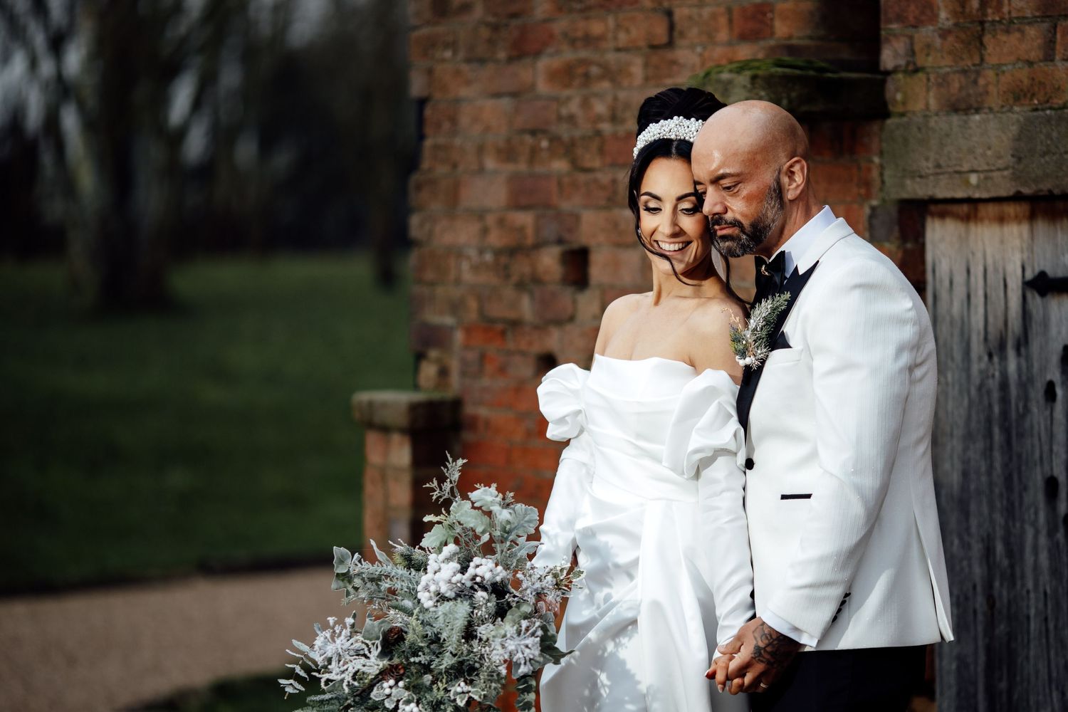 Newlyweds pose for romantic portraits against rustic brick wall with eucalyptus bouquet.