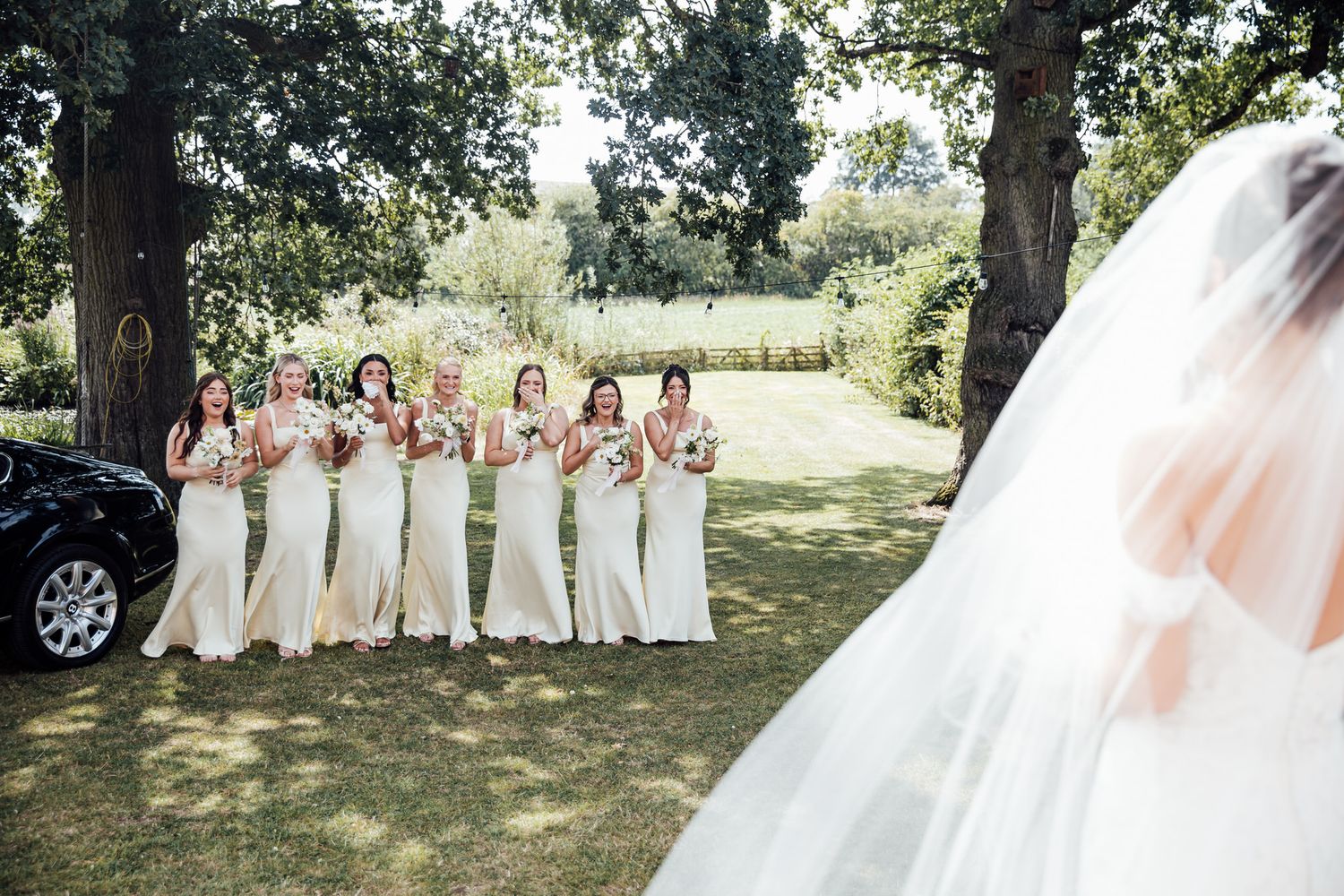 Bridesmaids in light-colored dresses pose together outdoors for wedding photos.