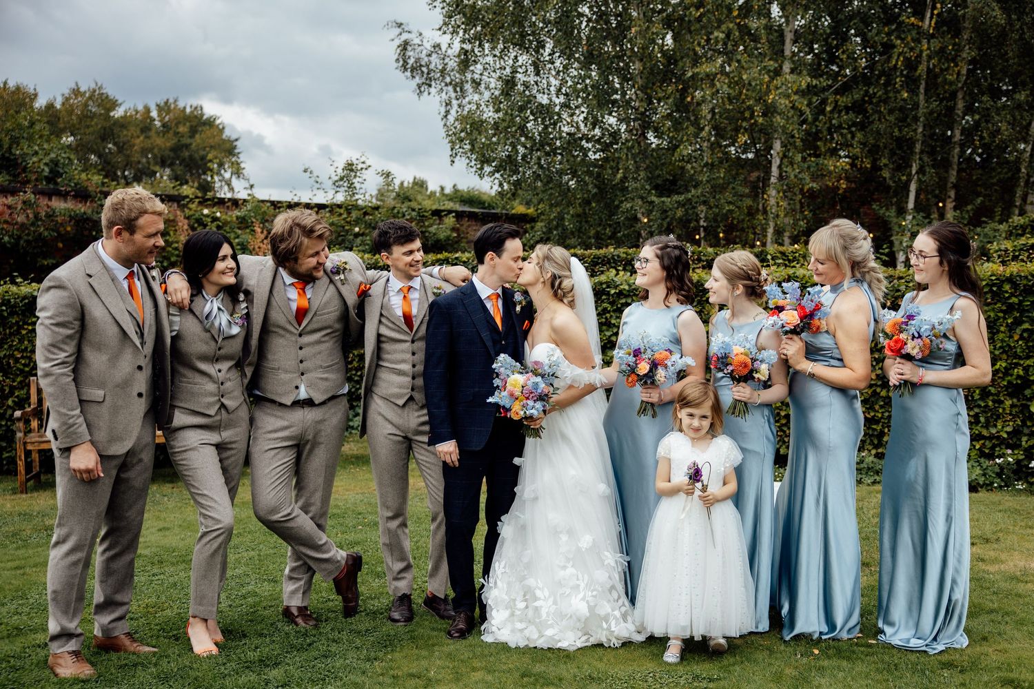 Wedding party poses outdoors in light blue dresses and gray suits on a sunny day.